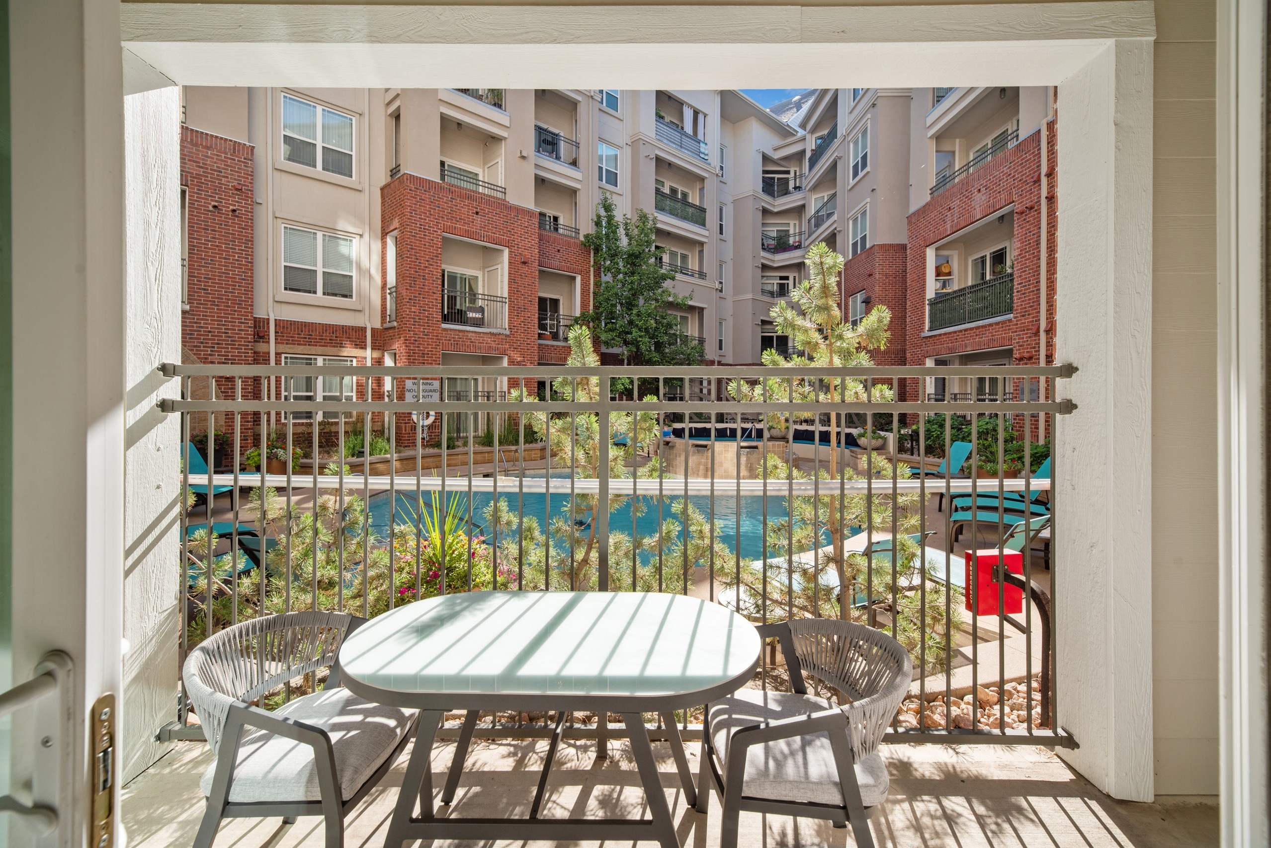 AMLI Park Avenue apartment patio with table and 2 chairs with tan railing and bars overlooking the courtyard pool
