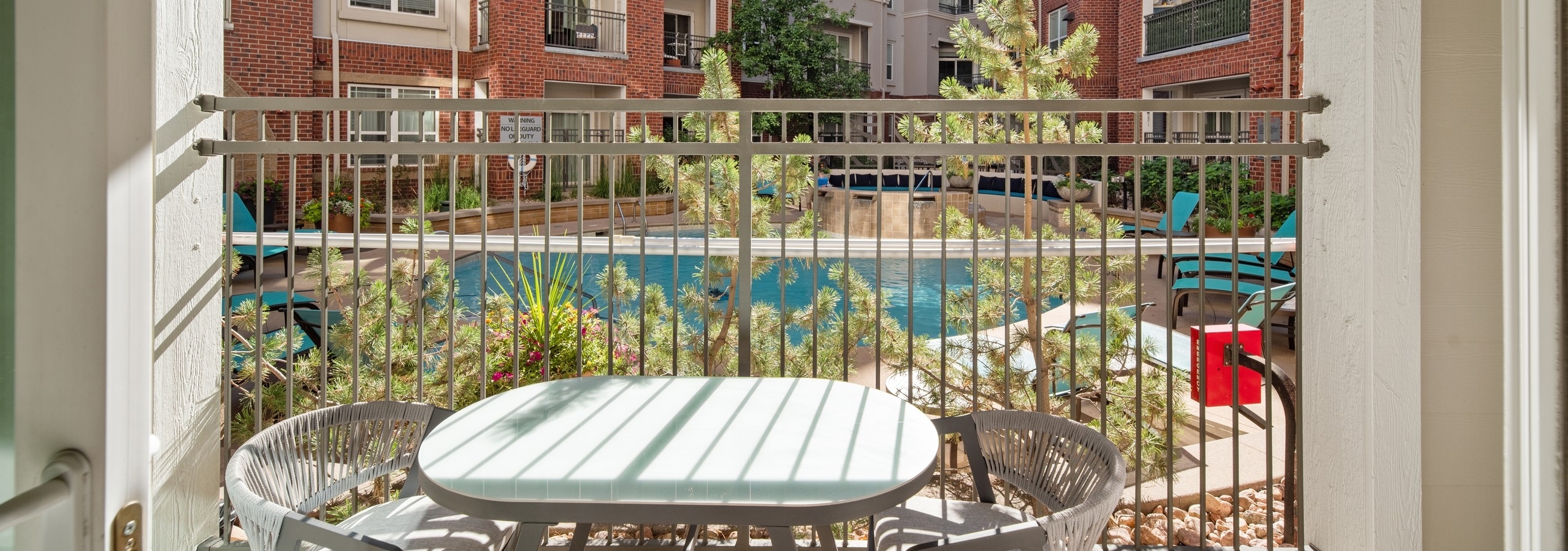 AMLI Park Avenue apartment patio with table and 2 chairs with tan railing and bars overlooking the courtyard pool