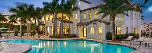 Dusk view of AMLI Doral pool with lights reflecting from the clubhouse surrounded by palm trees and lounge chairs