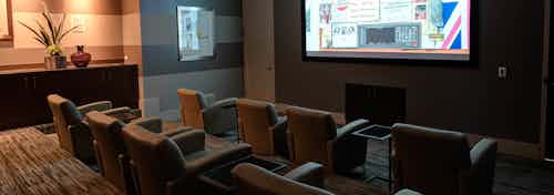 Interior view of theatre of AMLI River North with a video playing on a large screen TV and theatre seat rows in dim lighting