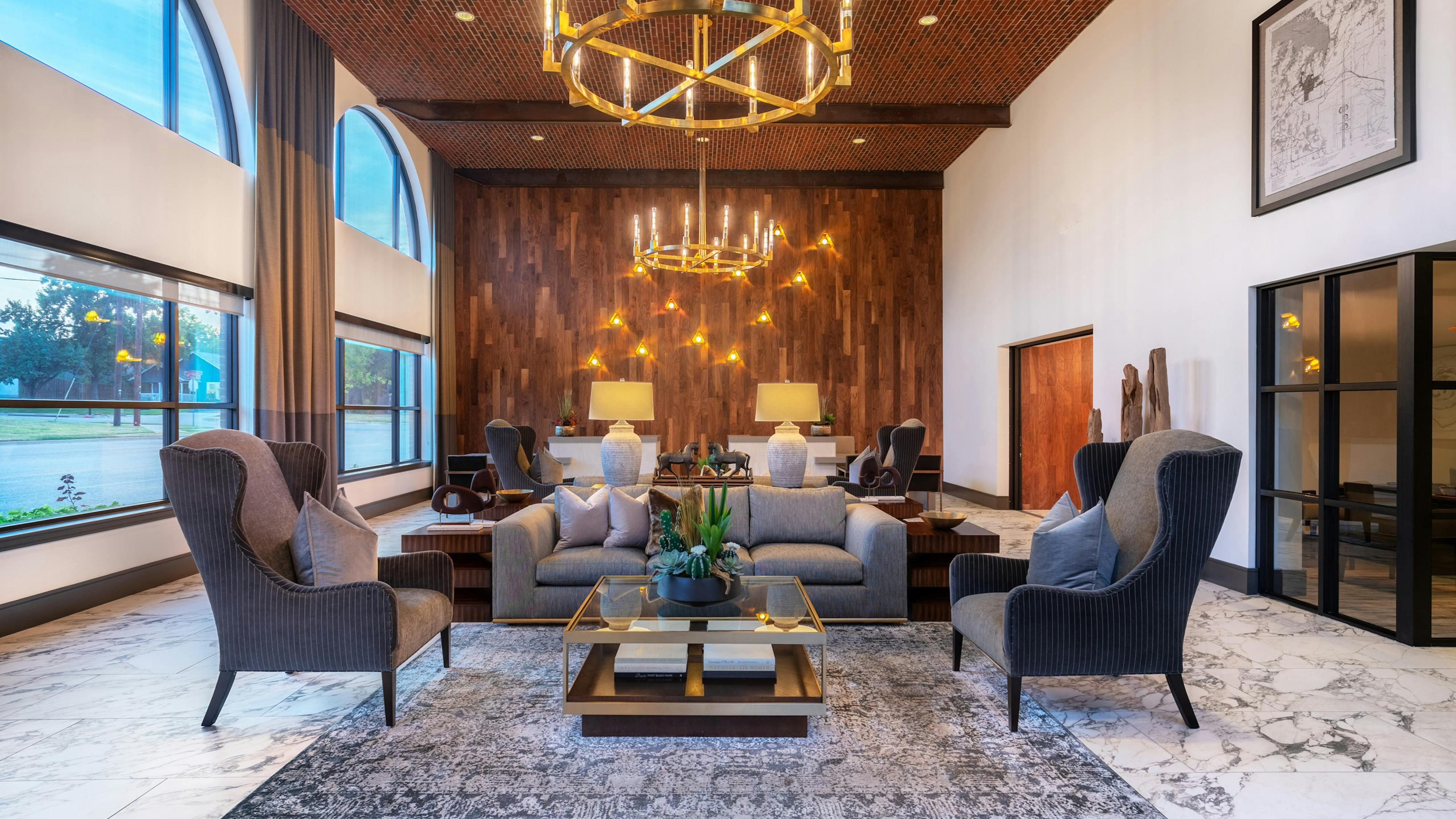 AMLI Grapevine clubroom with plush gray lounge seating and golden chandeliers and large windows and hardwood accent wall
