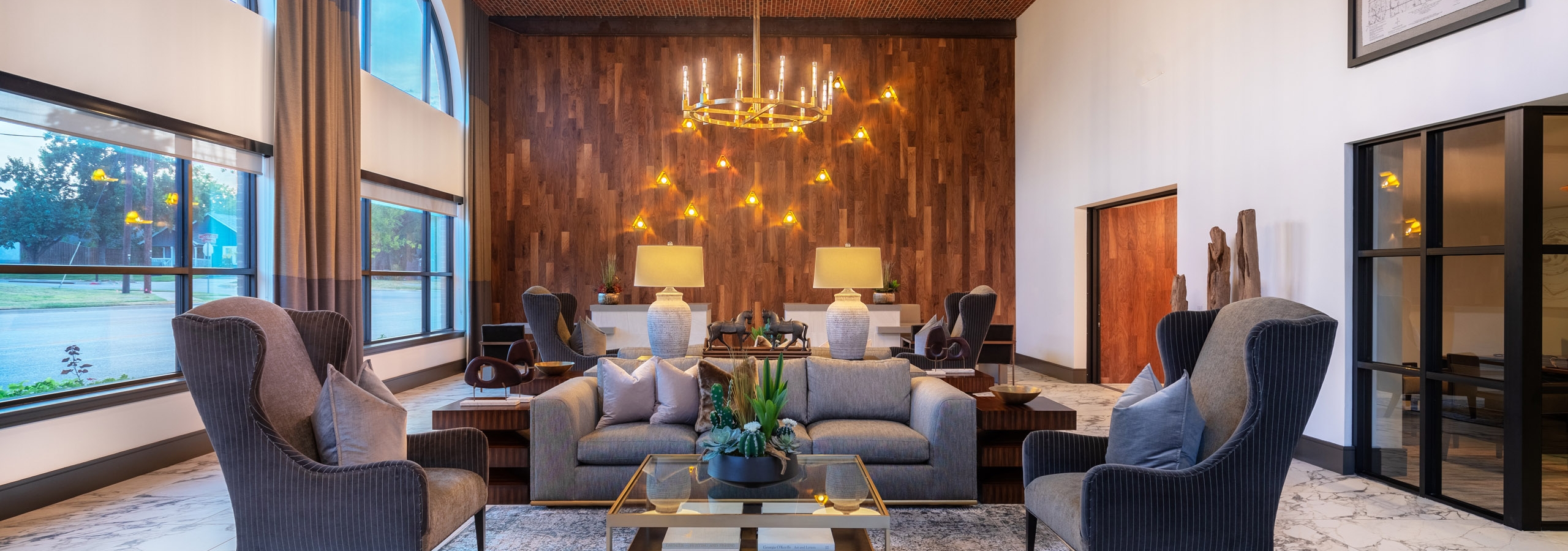AMLI Grapevine clubroom with plush gray lounge seating and golden chandeliers and large windows and hardwood accent wall