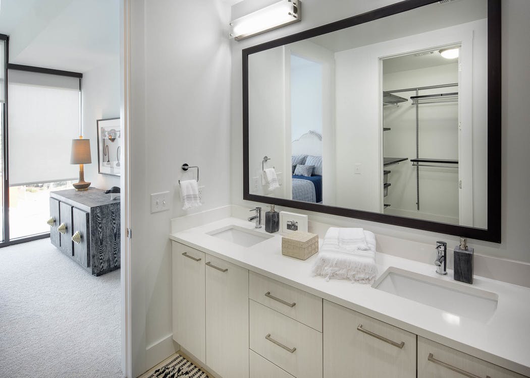 Interior of bathroom at AMLI 3464 with double vanity sink and white cabinets with open door leading to bedroom