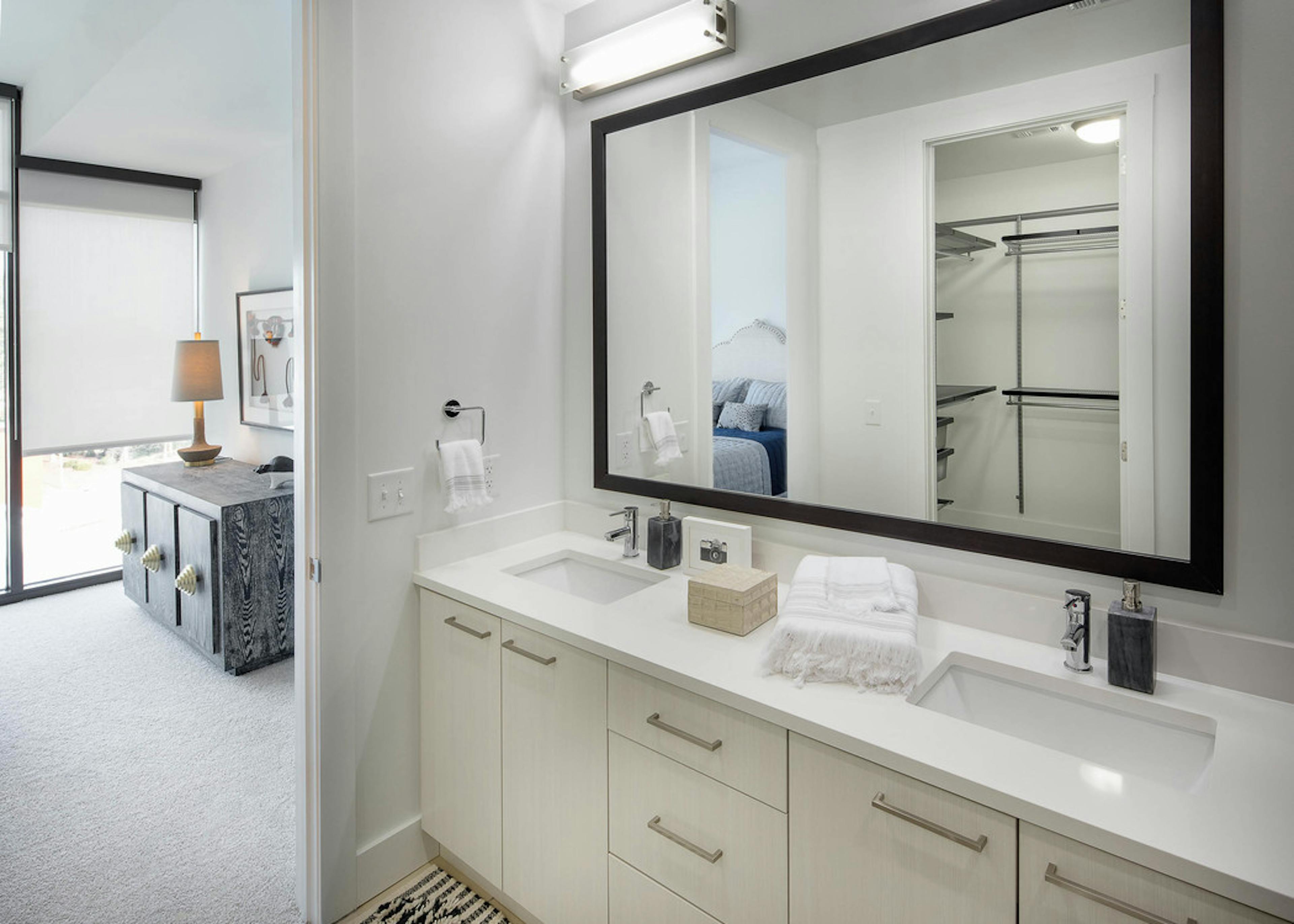 Interior of bathroom at AMLI 3464 with double vanity sink and white cabinets with open door leading to bedroom