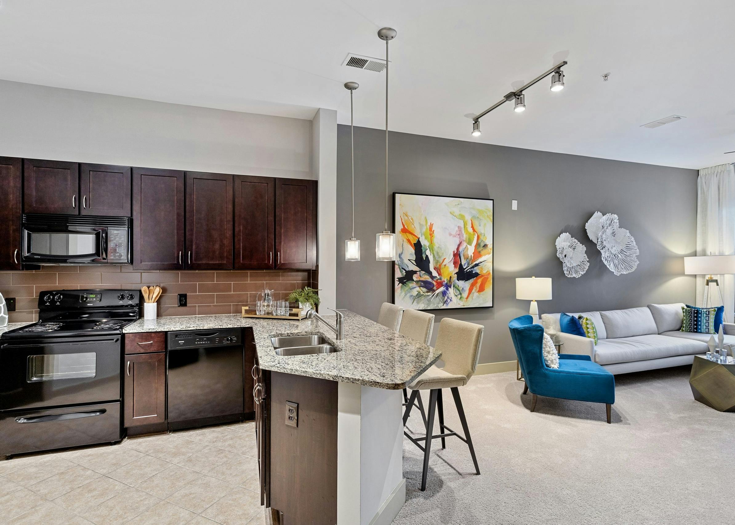 AMLI Parkside apartment kitchen and living area with dark wood cabinets and granite counters and peek into the living area