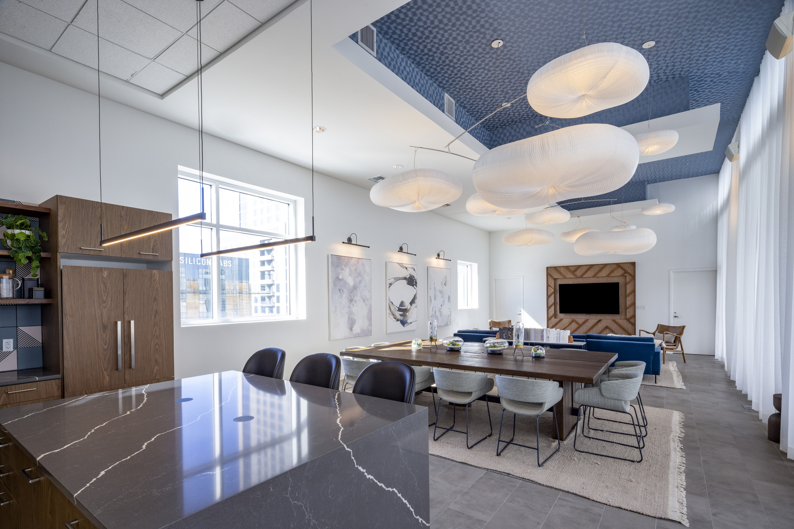 AMLI on 2nd resident lounge with spacious island and wooden table beneath modern light fixtures and geometric blue ceiling