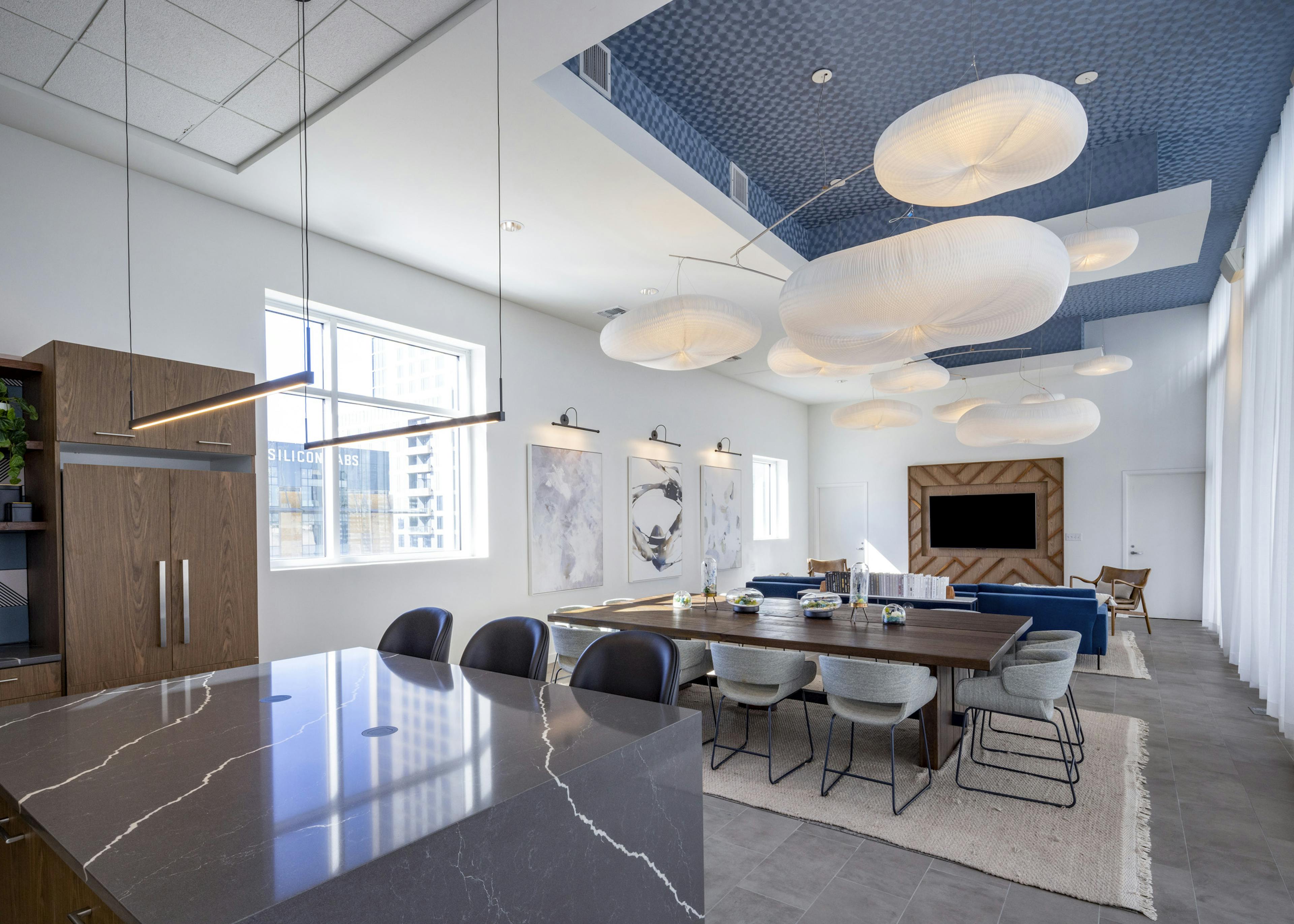 AMLI on 2nd resident lounge with spacious island and wooden table beneath modern light fixtures and geometric blue ceiling