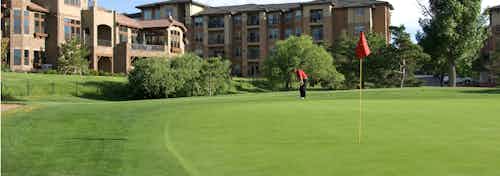 An individual golfing on a putting green at the Club at Inverness golf course with AMLI Inverness apartment building in view