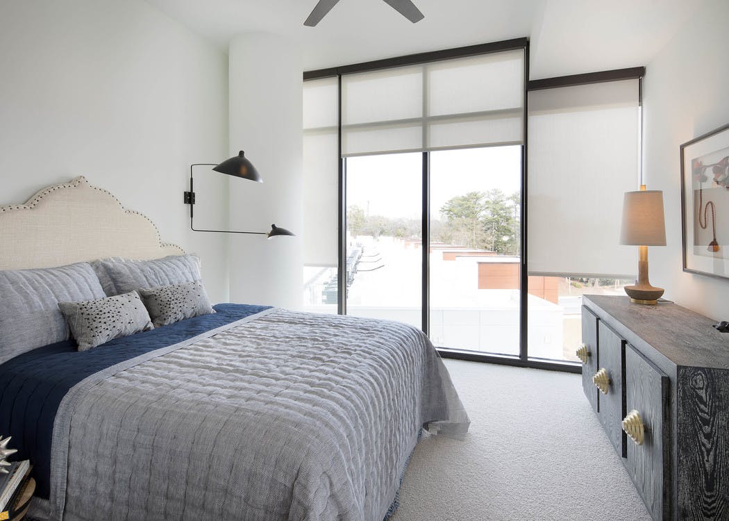 Bedroom at AMLI 3464 with white walls and grey and dark blue bedding with floor to ceiling windows with a daytime view