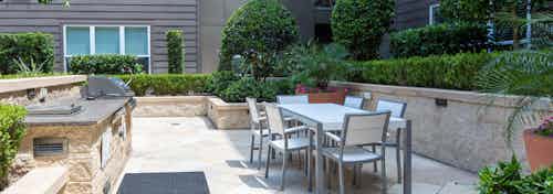 Daytime view of outdoor dining and grilling area at AMLI River Oaks apartment building with lush greenery and potted flowers