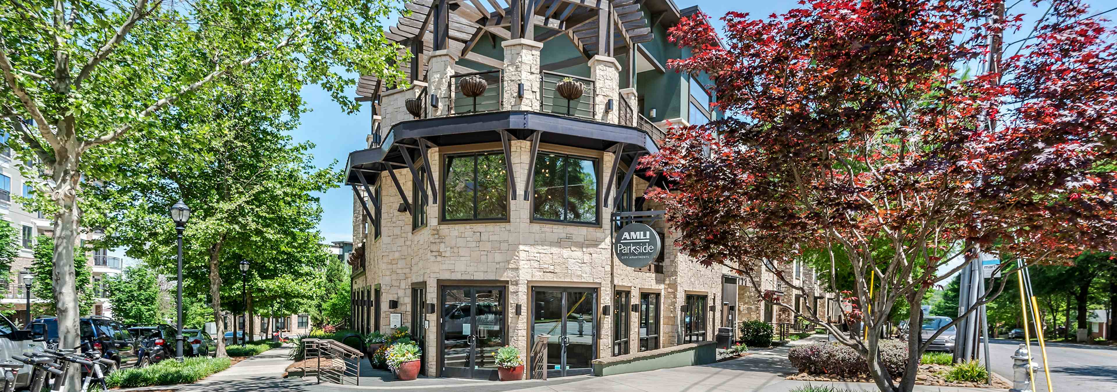 Exterior of AMLI Parkside apartment community entry way with stone façade and luscious trees on both sides on a sunny day