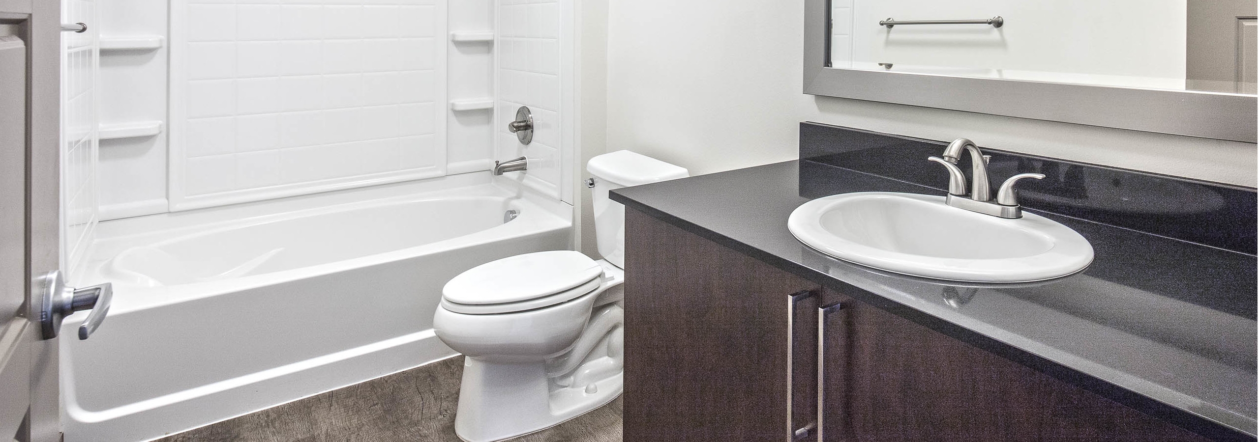 Interior view of an AMLI Mark24 apartment bathroom with white walls black quartz counter top and large shower tub combination
