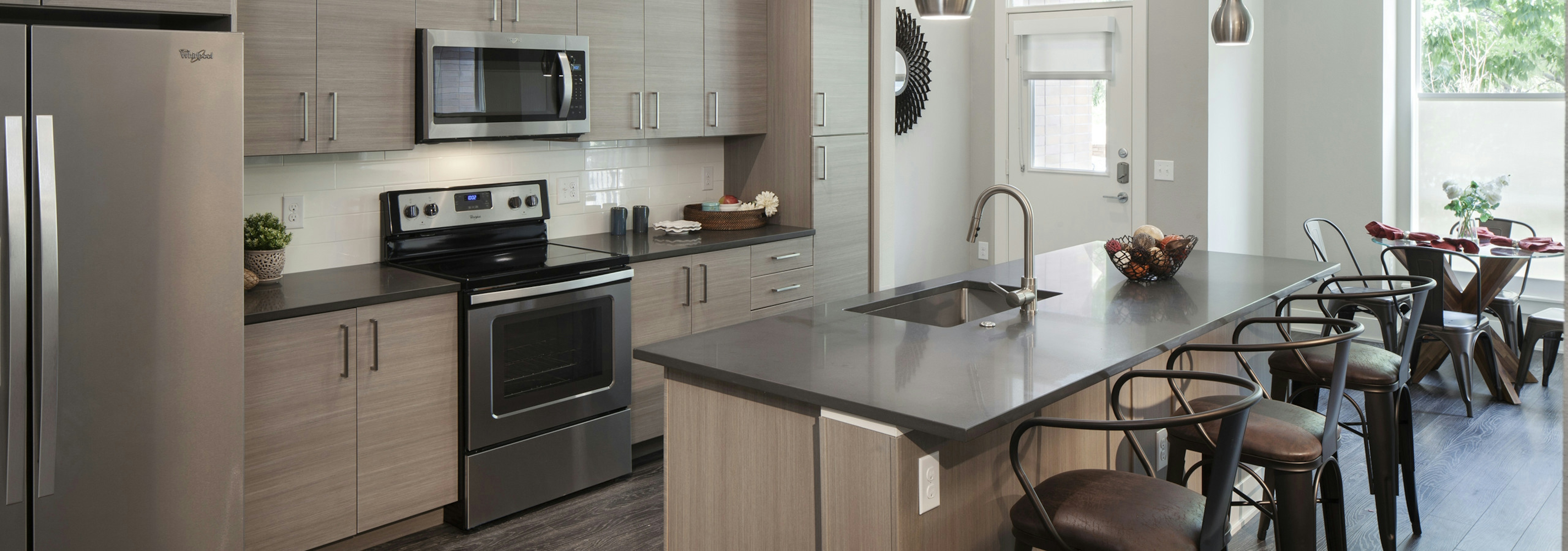 Interior view of AMLI Riverfront Green apartment townhome kitchen with kitchen island and bar chairs and view of living room