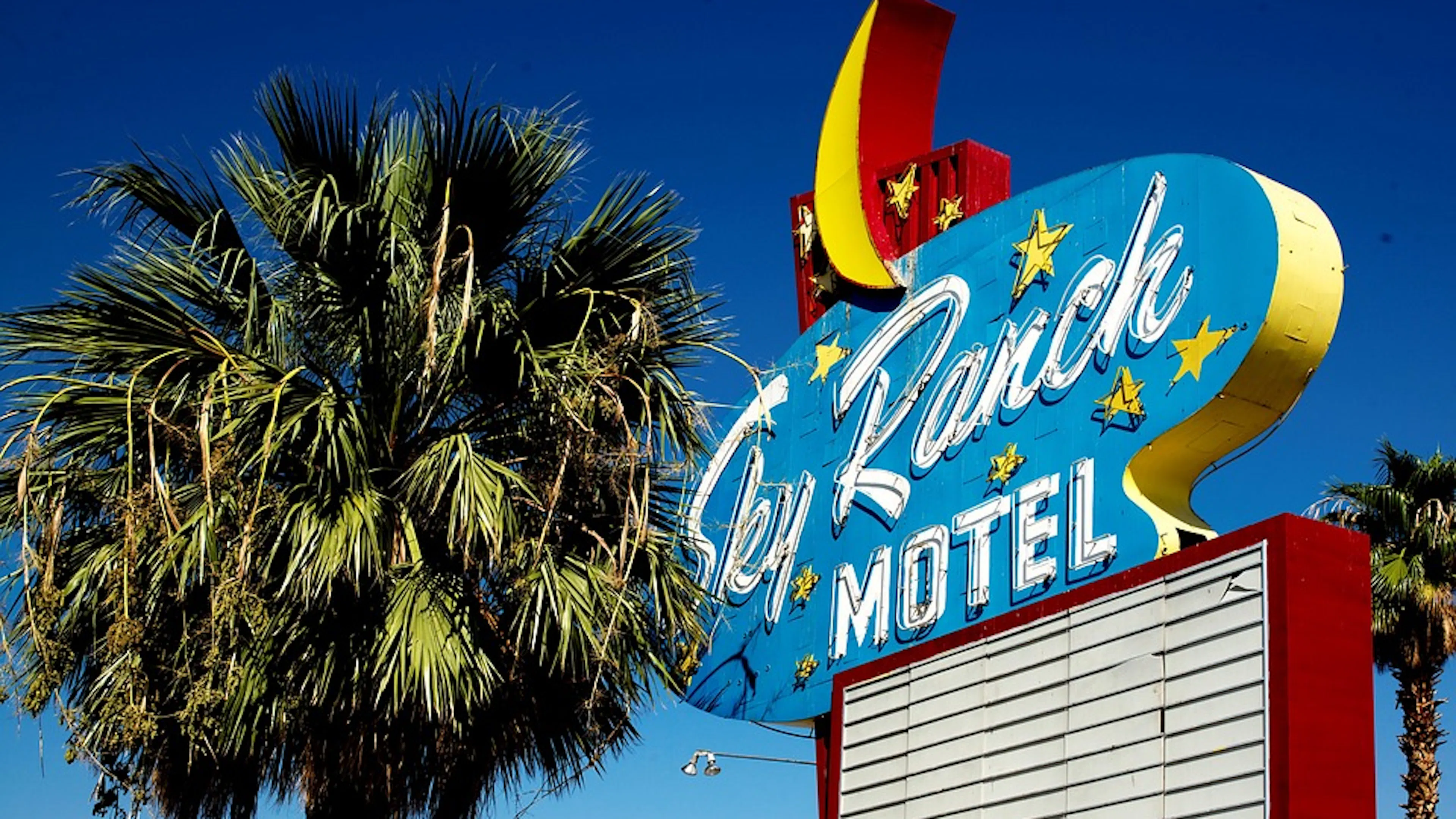 A retro motel sign saying Sky Ranch Motel next to a palm tree