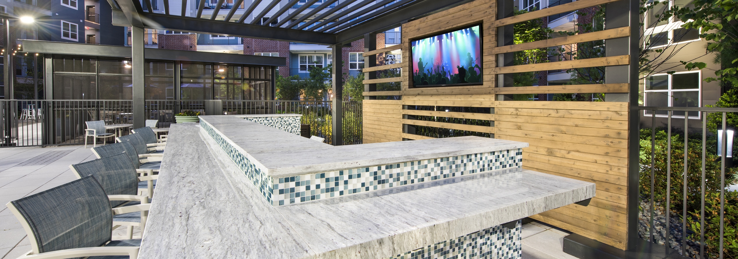 Evening view of AMLI Decatur open layout pool bar with blue and white small tiles and high stools and built in television