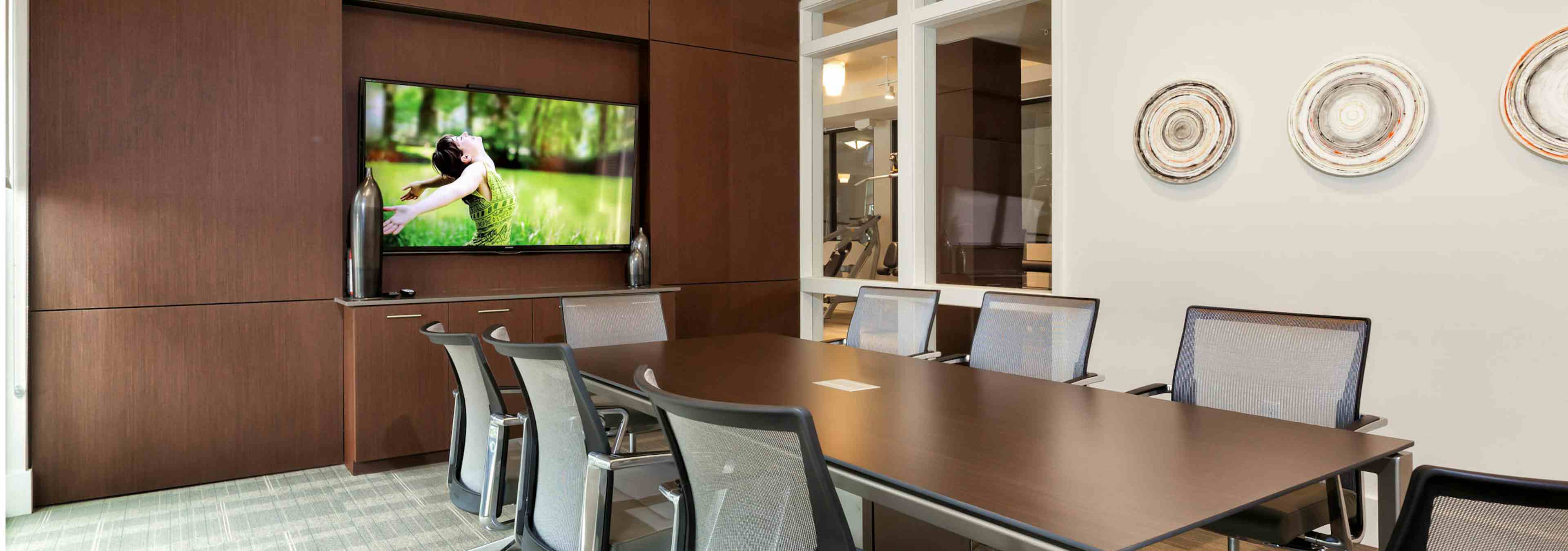 AMLI West Plano conference room with a TV hanging on a dark brown accent wall with a long wooden desk with grey office chairs