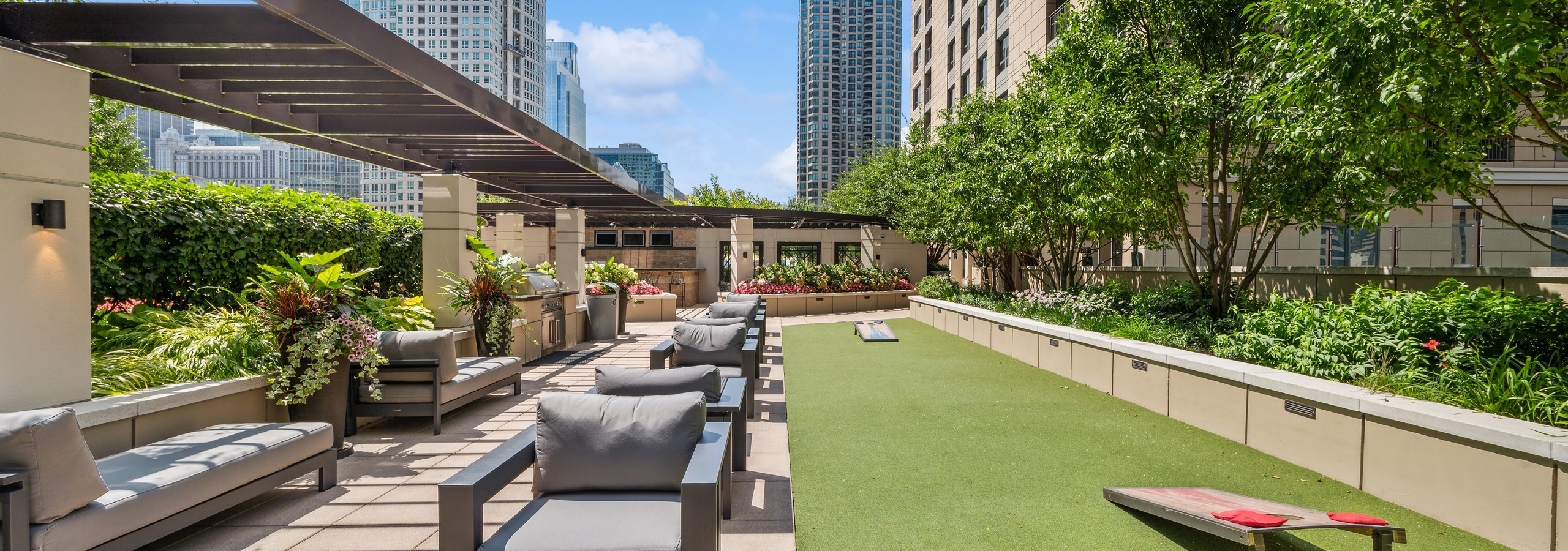 Daytime exterior of AMLI River North rooftop with ample lounge seating and turf space with cornhole boards and view of city