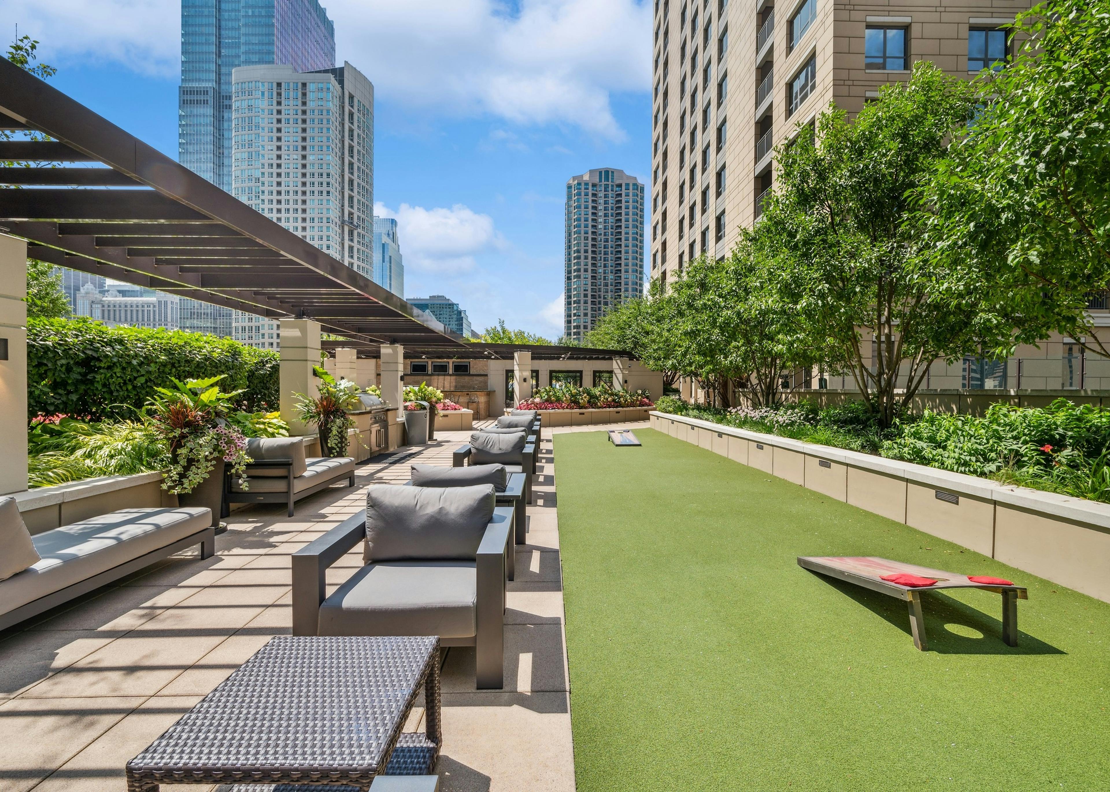 Daytime exterior of AMLI River North rooftop with ample lounge seating and turf space with cornhole boards and view of city
