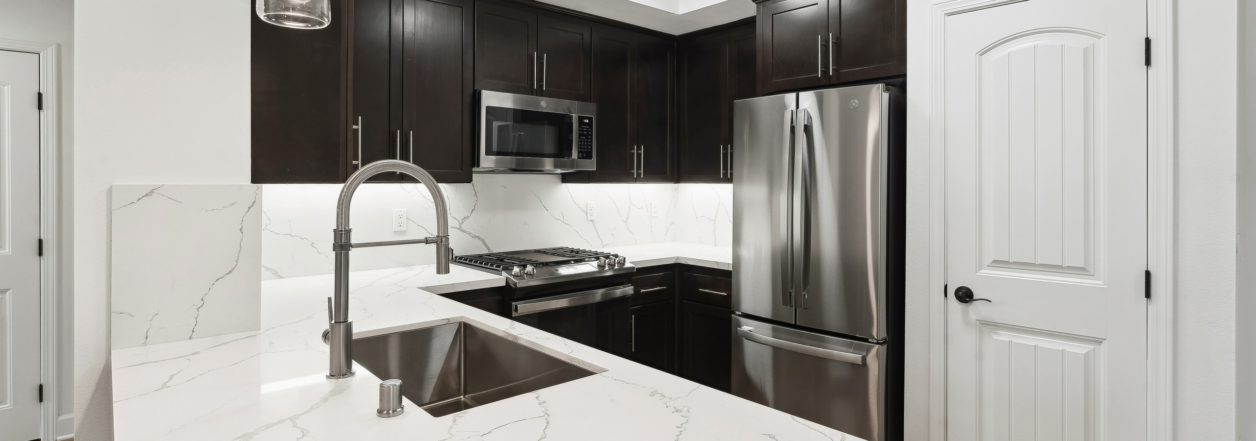 AMLI Spanish Hills apartment kitchen with wrap around white quartz countertop and dark brown cabinets and stainless appliances