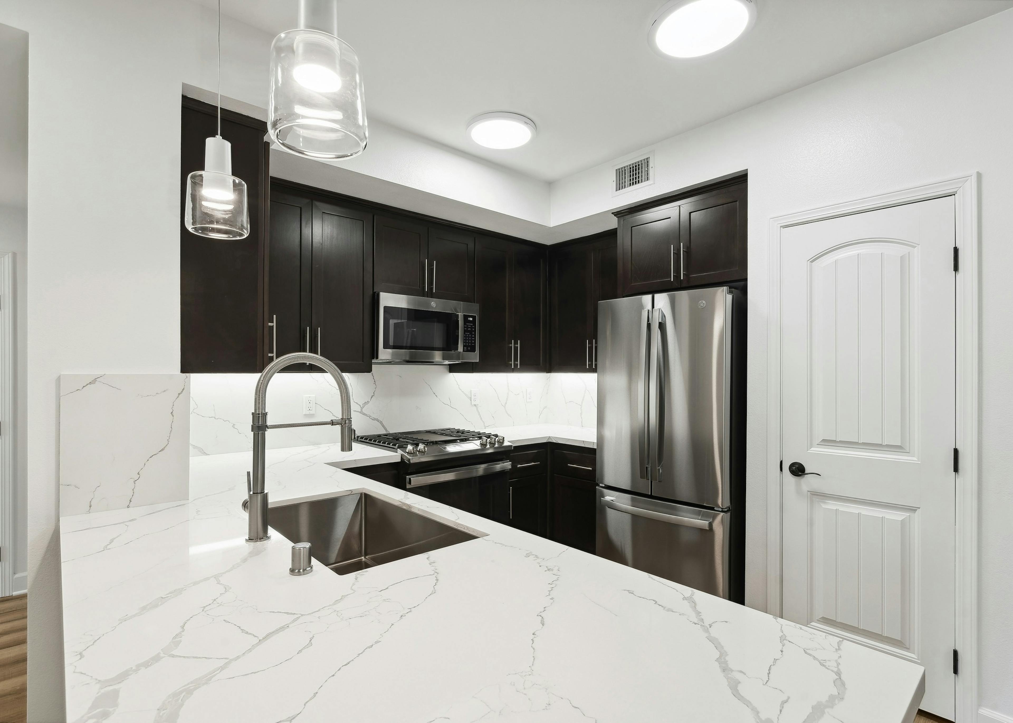 AMLI Spanish Hills apartment kitchen with wrap around white quartz countertop and dark brown cabinets and stainless appliances
