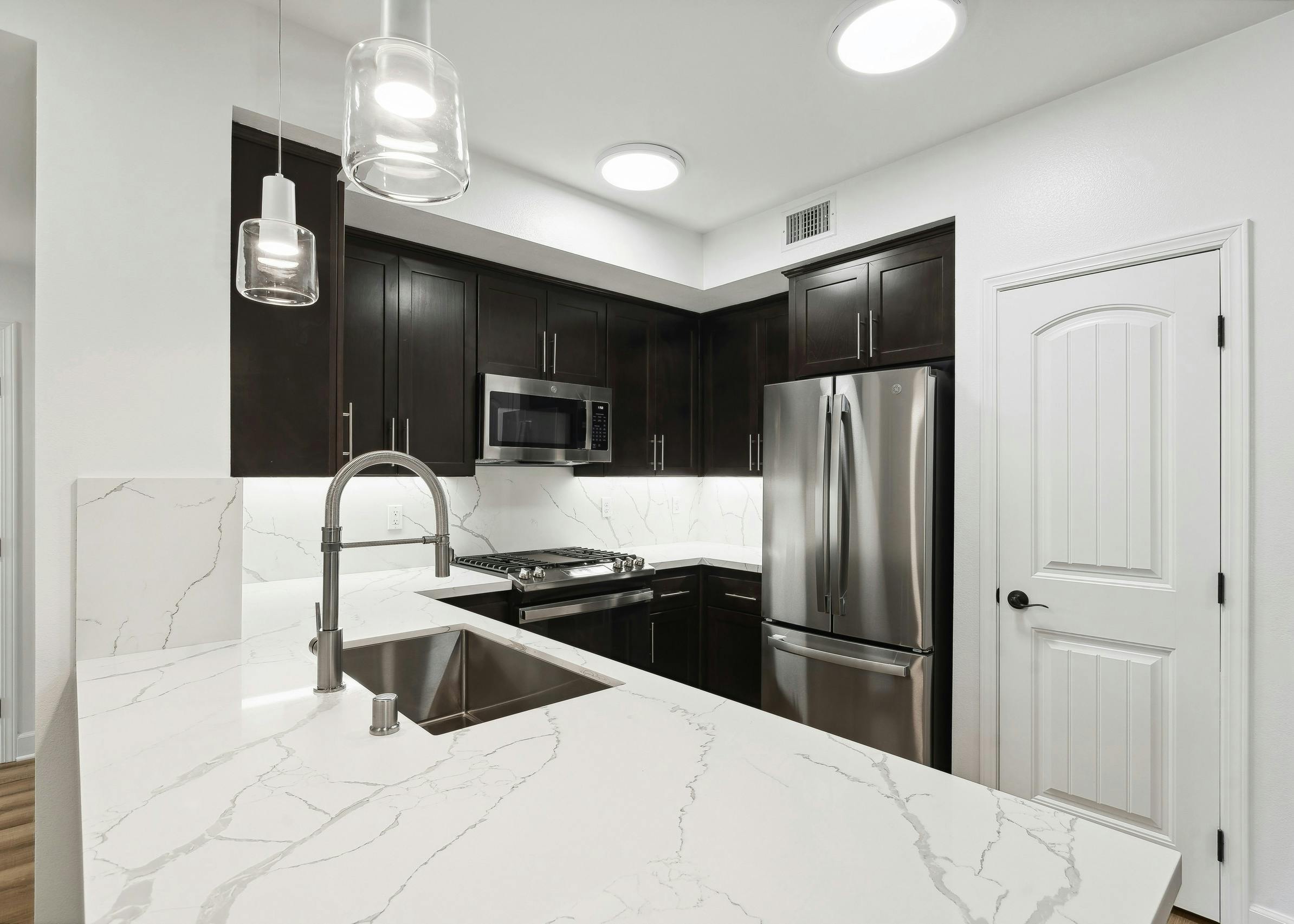 AMLI Spanish Hills apartment kitchen with wrap around white quartz countertop and dark brown cabinets and stainless appliances