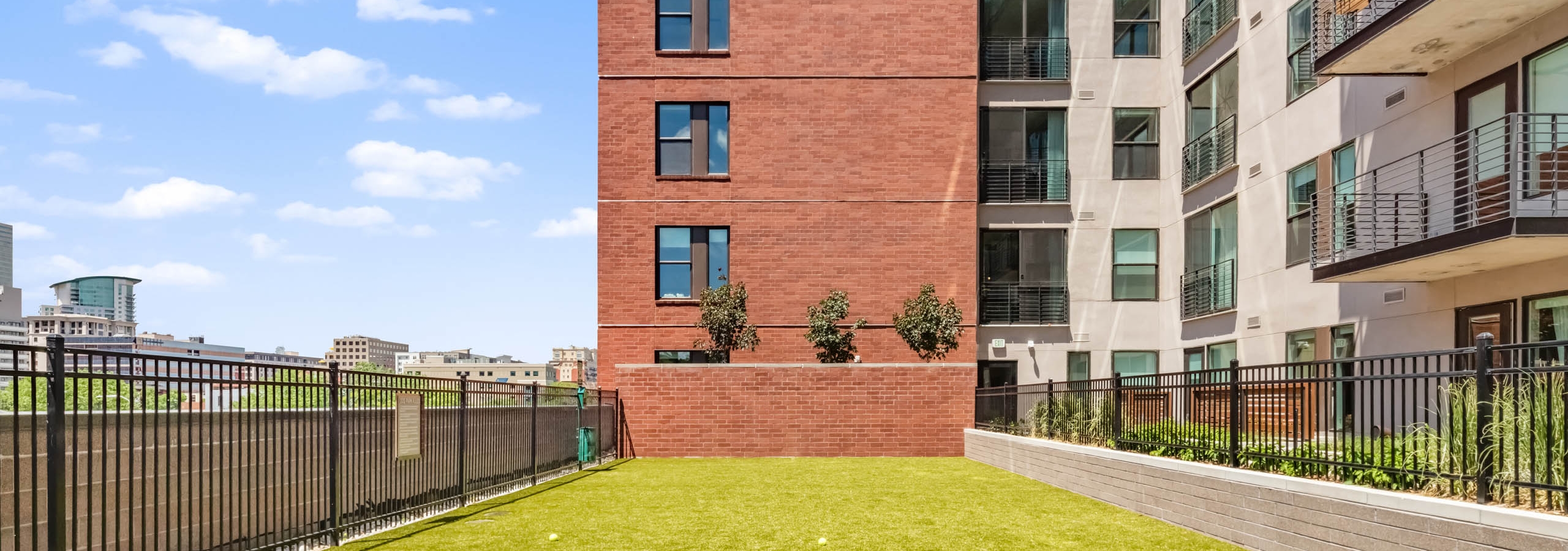 Spacious outdoor pet park at AMLI at Uptown with green turf surrounded by exterior building facade and vibrant blue sky