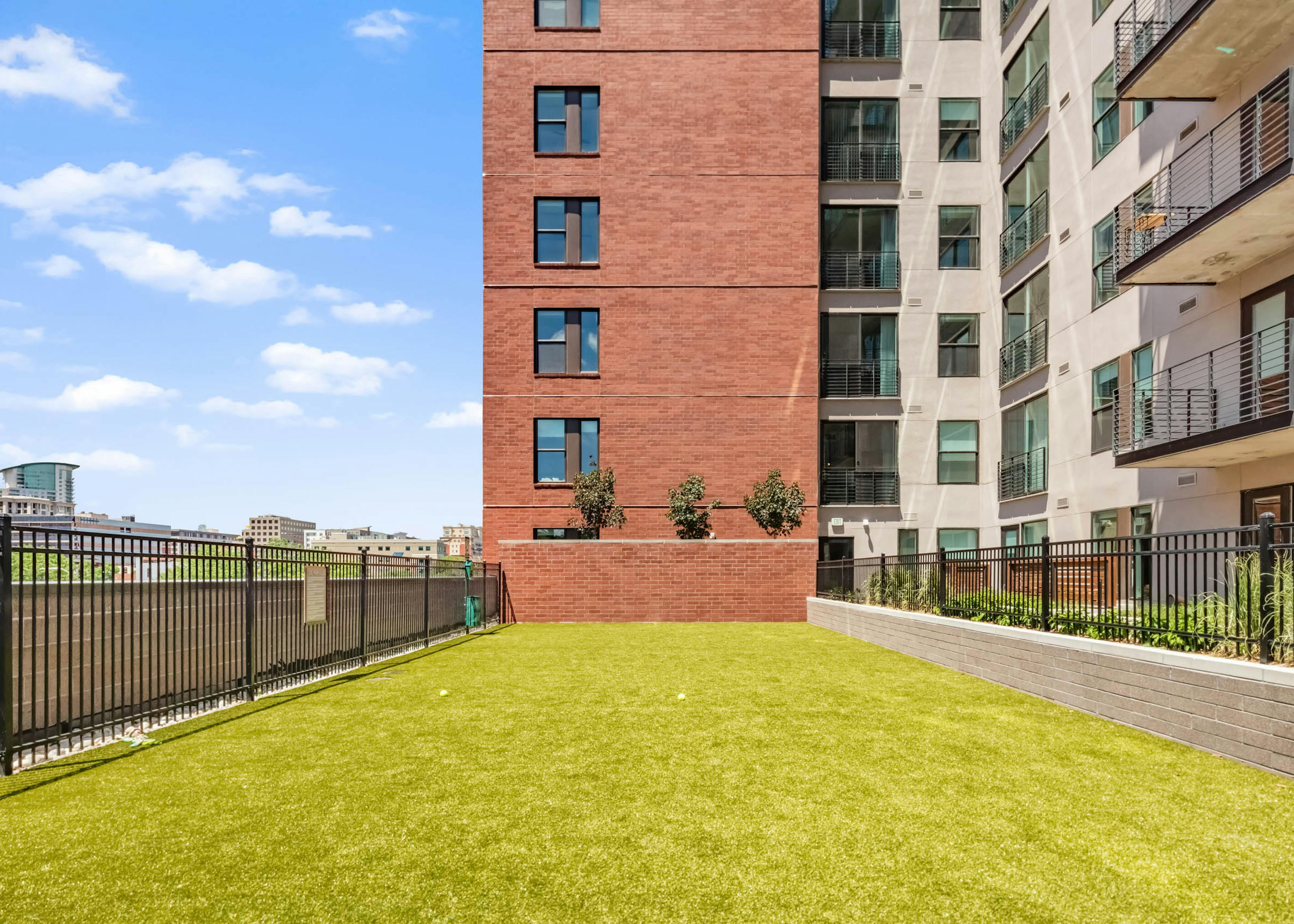 Spacious outdoor pet park at AMLI at Uptown with green turf surrounded by exterior building facade and vibrant blue sky