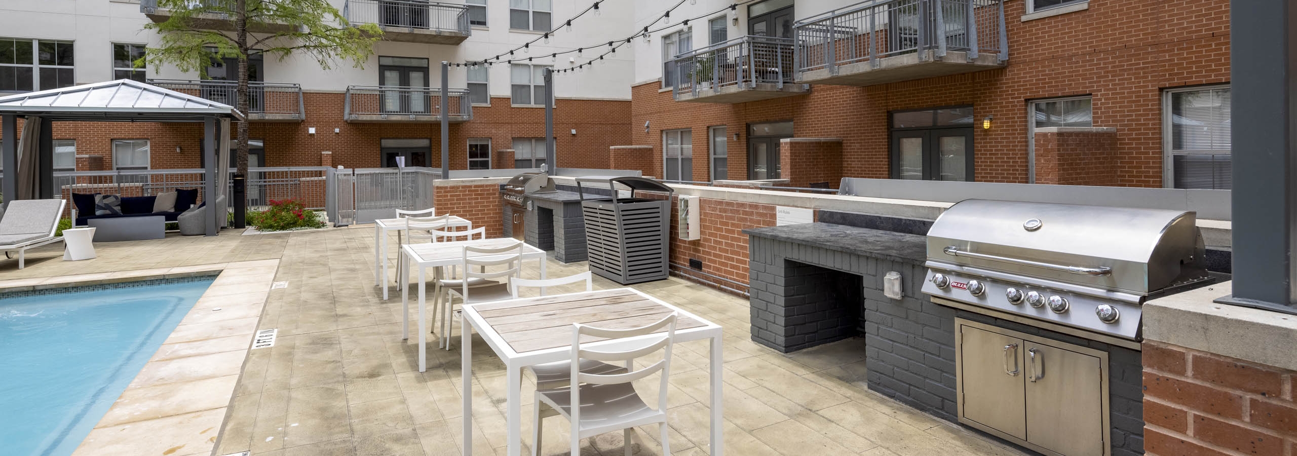Poolside grill at AMLI Downtown with two stainless grills and white dining furniture with string lights hanging above