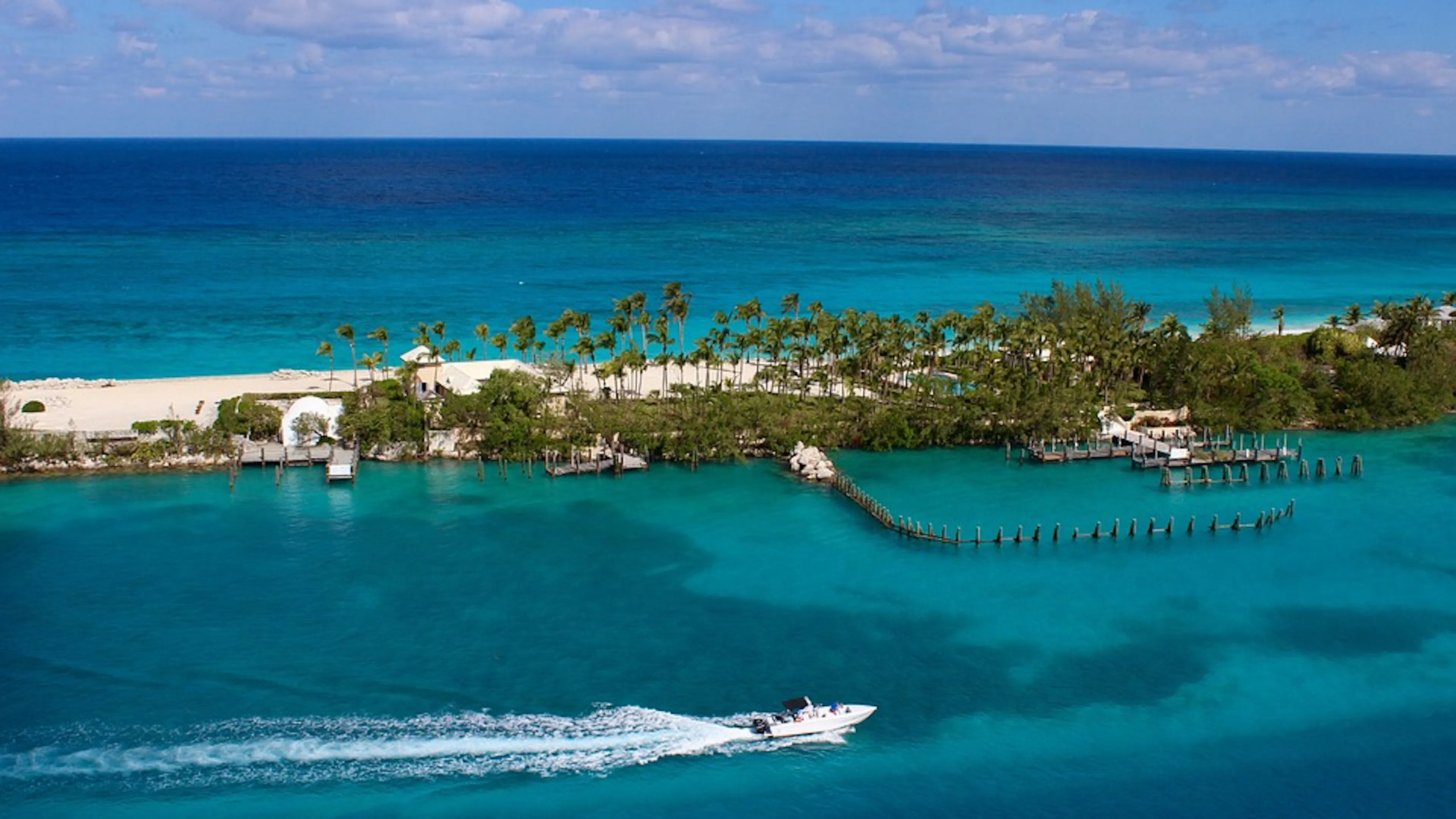A narrow island in the Bahamas surrounded by clear blue water and covered in white sands and green palms