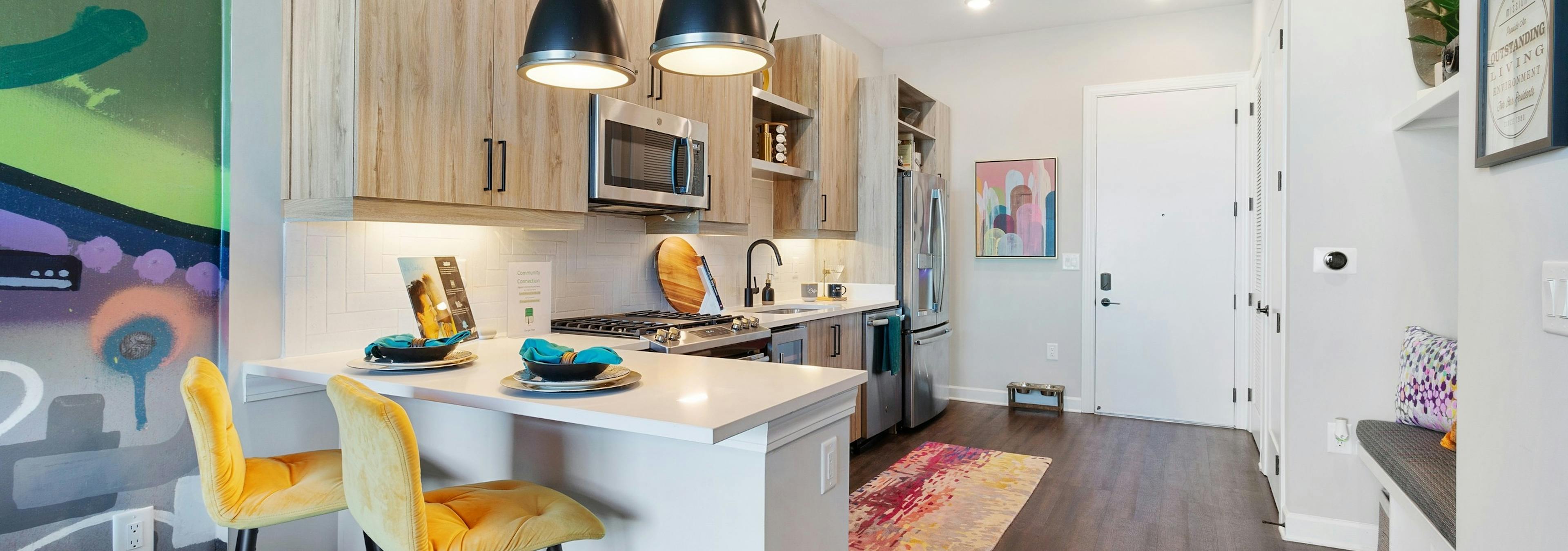 Interior view of kitchen with breakfast counter and yellow barstools and colorful artwork pieces at AMLI Westside apartments