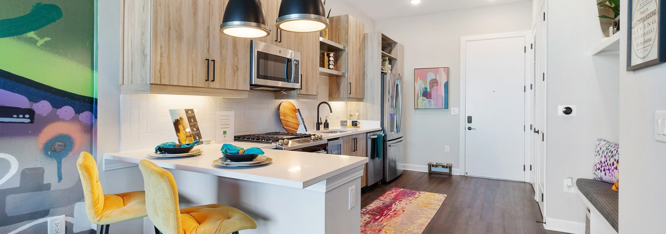 Interior view of kitchen with breakfast counter and yellow barstools and colorful artwork pieces at AMLI Westside apartments