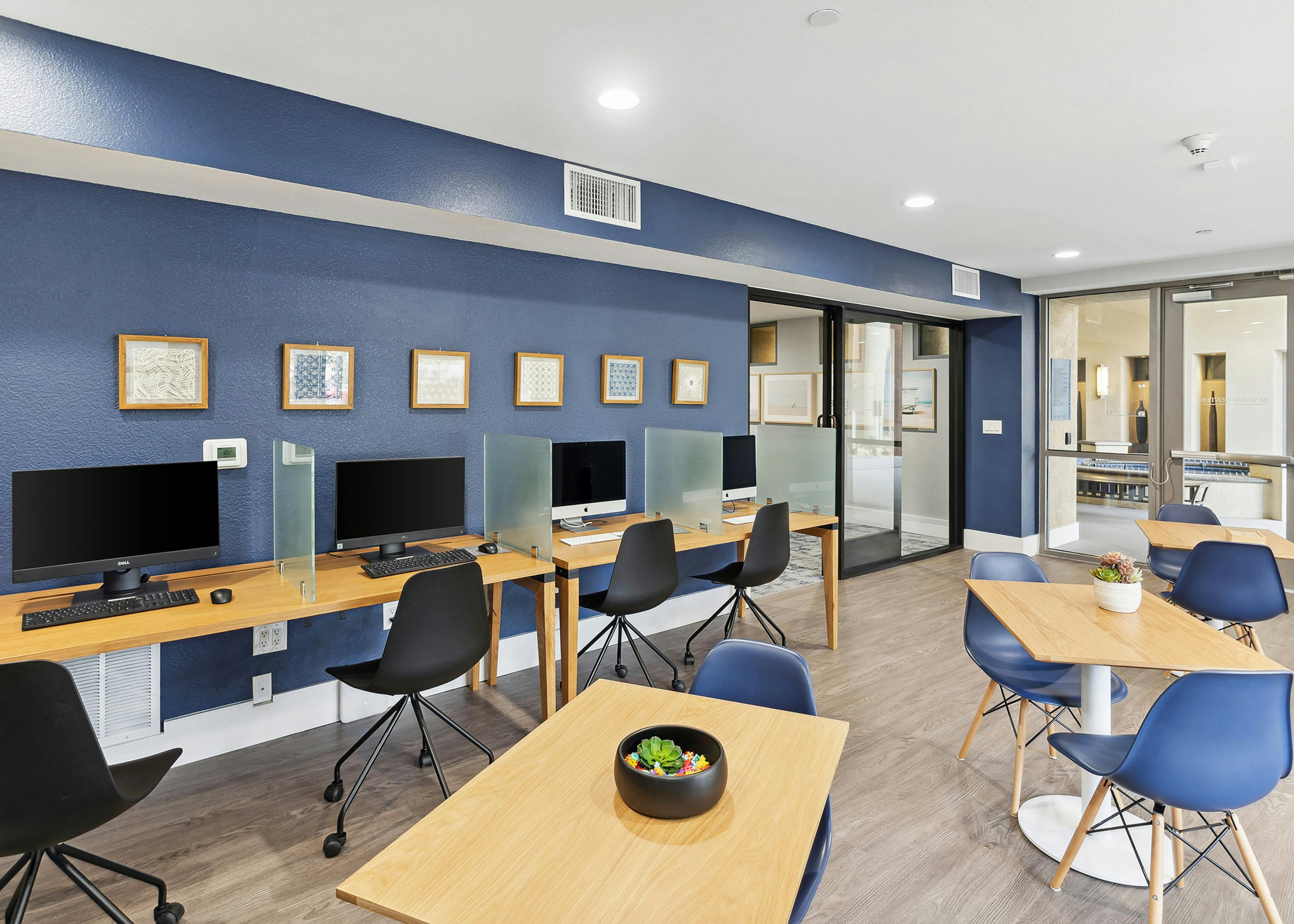Daytime view of the business center with four computer stations and wood tables with blue chairs at AMLI Warner Center
