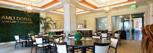 Interior party room at AMLI Doral with bright orange wall accents, ornate light fixtures, tables, chairs and faux grass wall