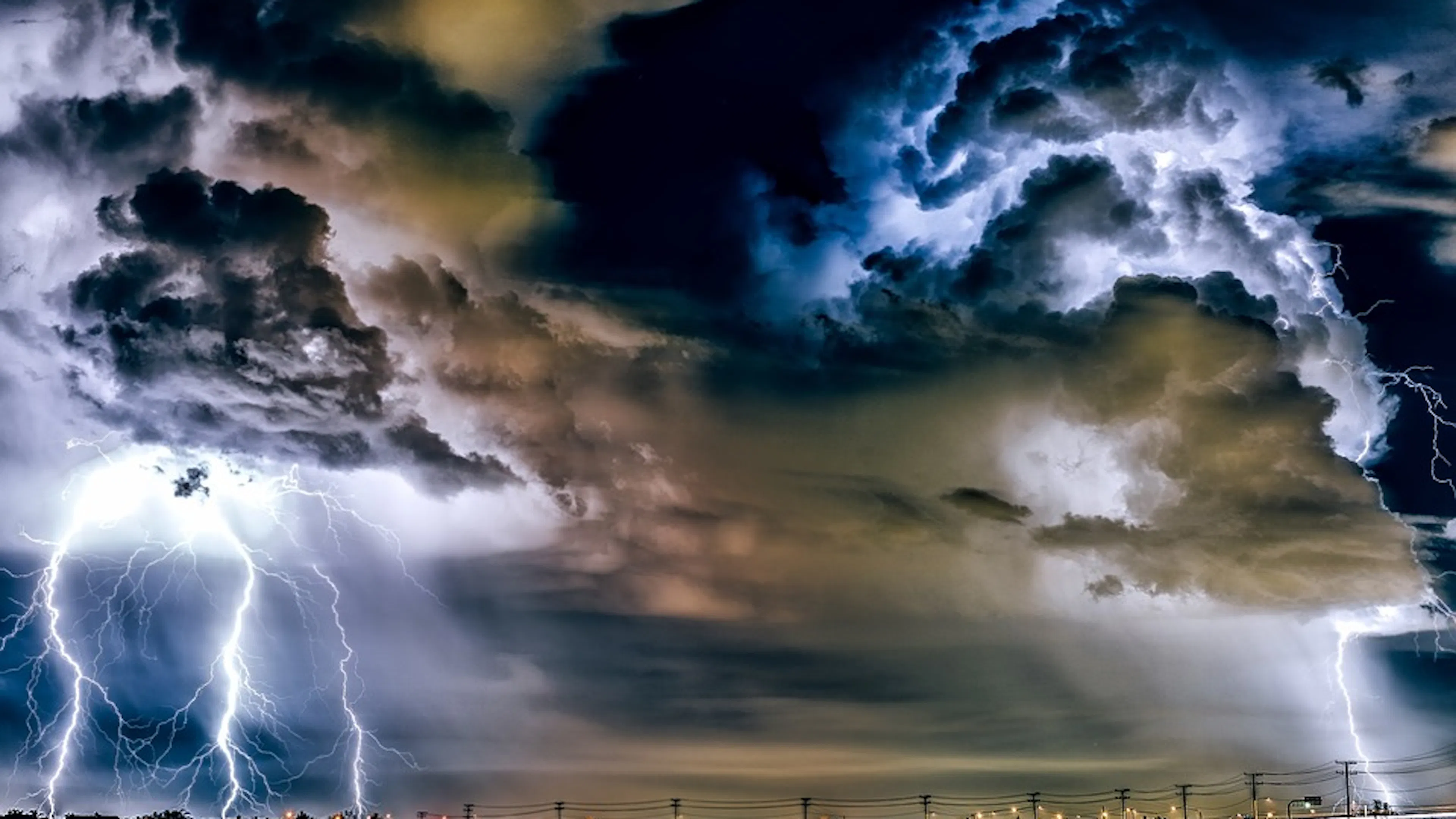 A massive lightening storm striking over a well-lit town at night time