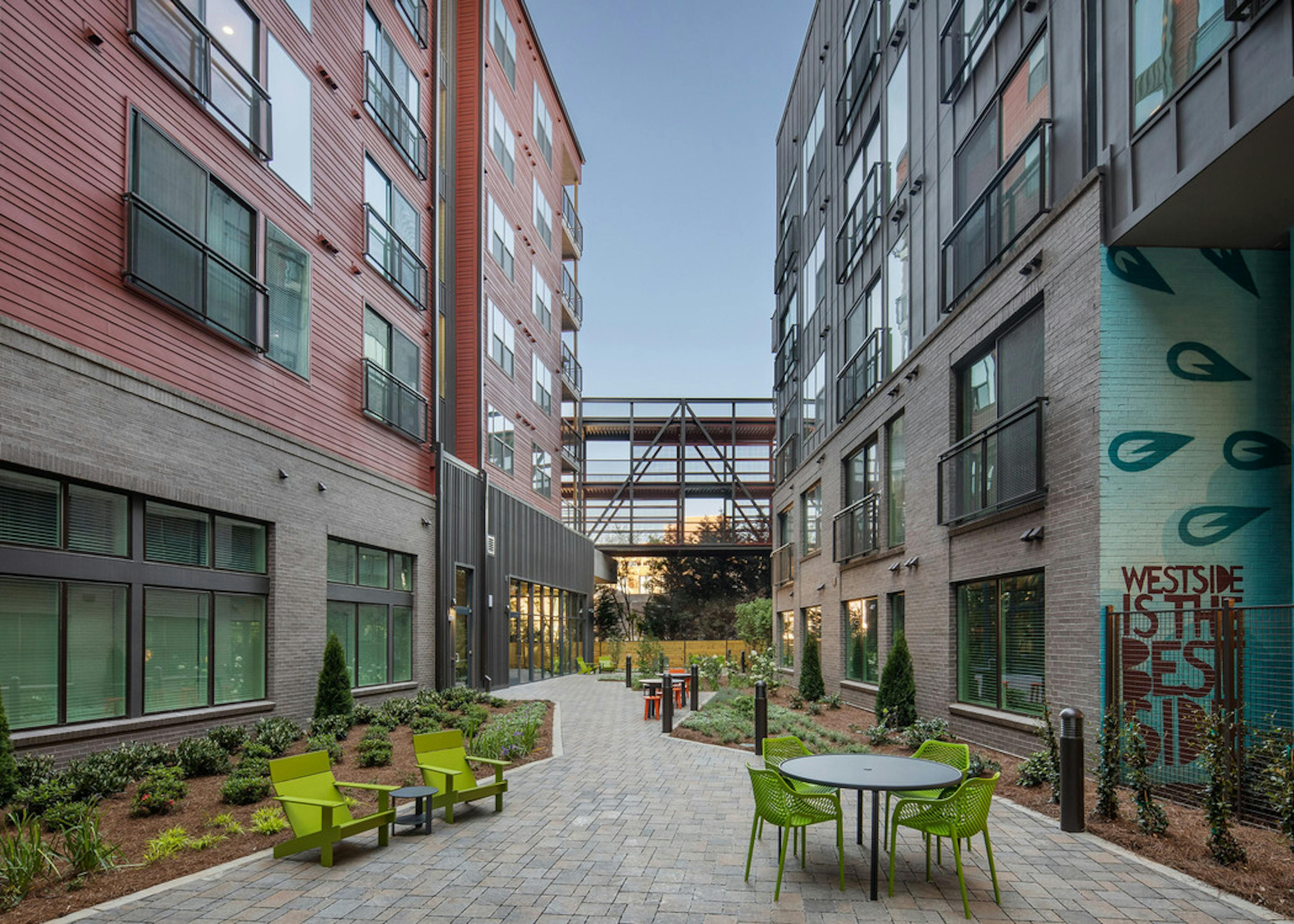 Daytime exterior view of AMLI Westside landscaped courtyard with various colorful seating options on a brick pathway