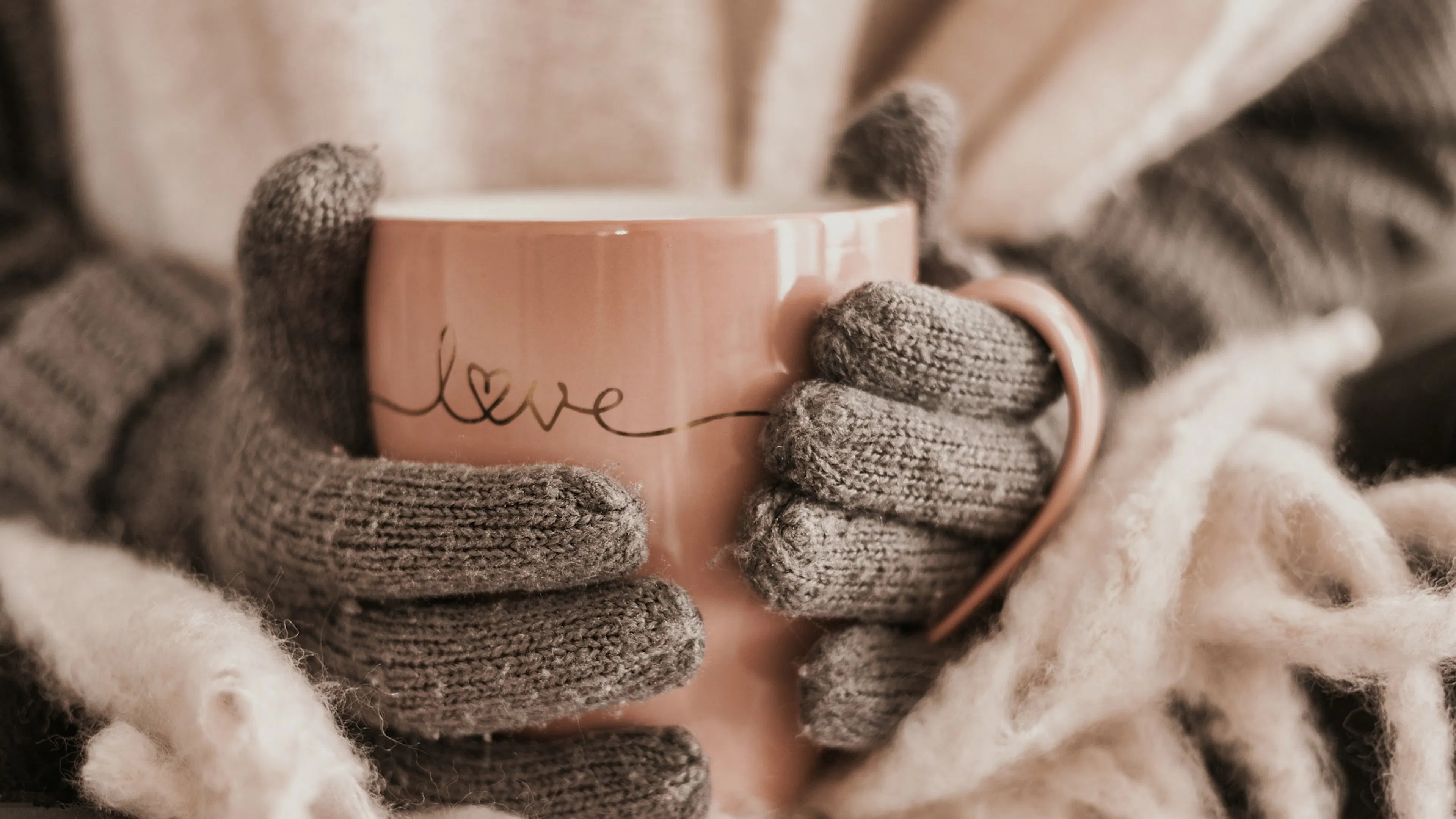 tan gloved hands wrapped around pink love mug with scarf