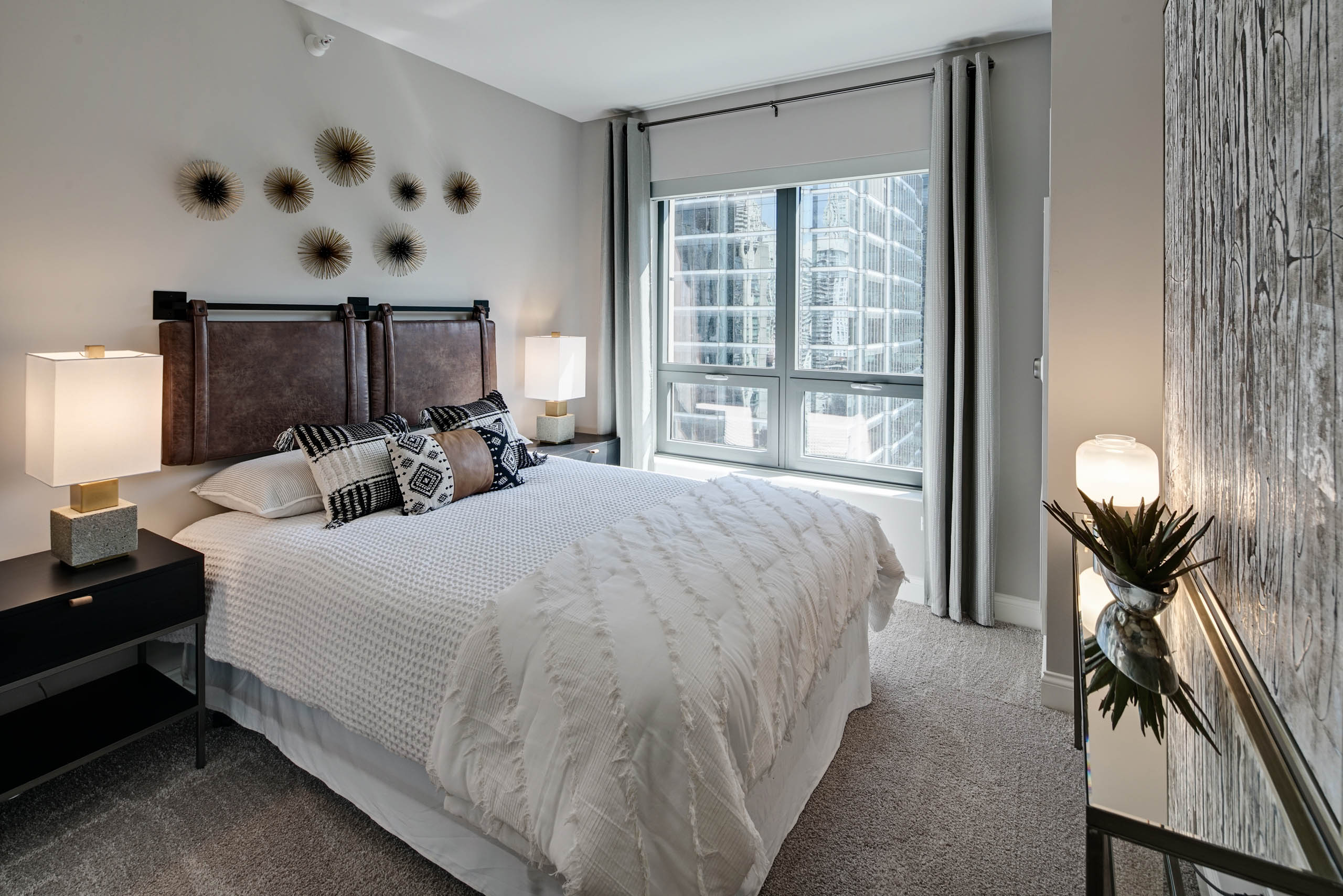 AMLI River North apartment bedroom with neutral walls and grey carpeting with bold decor and a window showing light city view