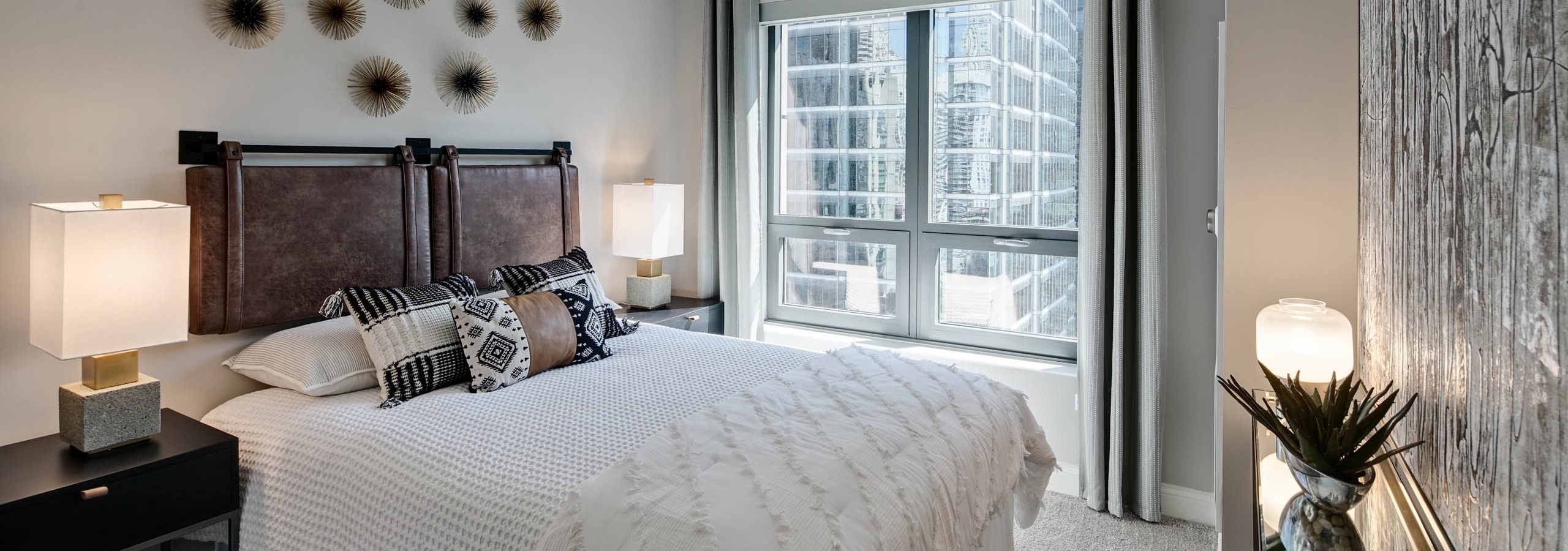 AMLI River North apartment bedroom with neutral walls and grey carpeting with bold decor and a window showing light city view