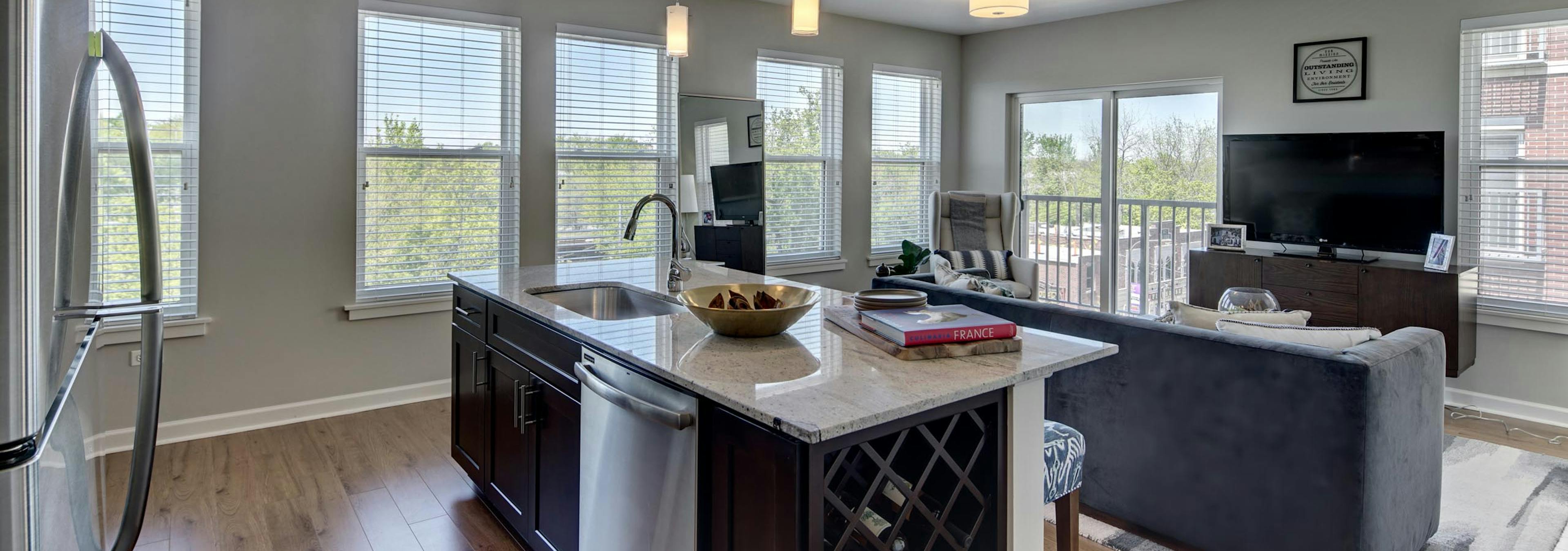 Sleek granite island in an AMLI Evanston apartment kitchen with view of living area in background surrounded by bright windows