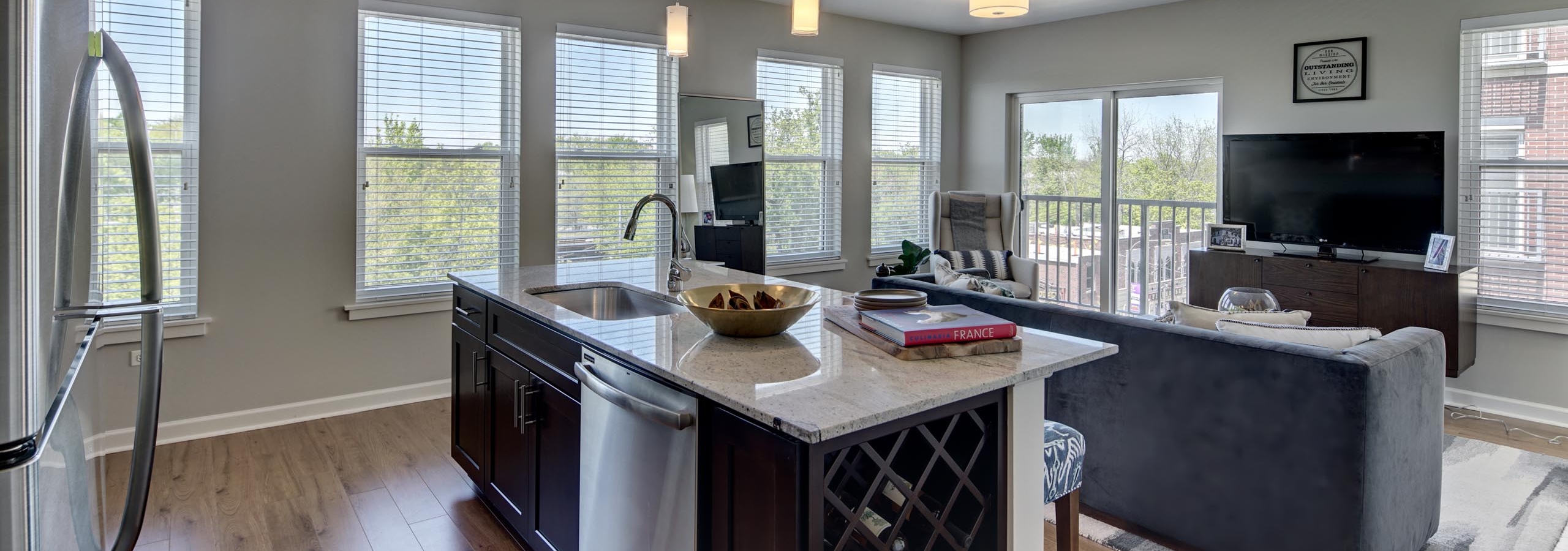 Sleek granite island in an AMLI Evanston apartment kitchen with view of living area in background surrounded by bright windows