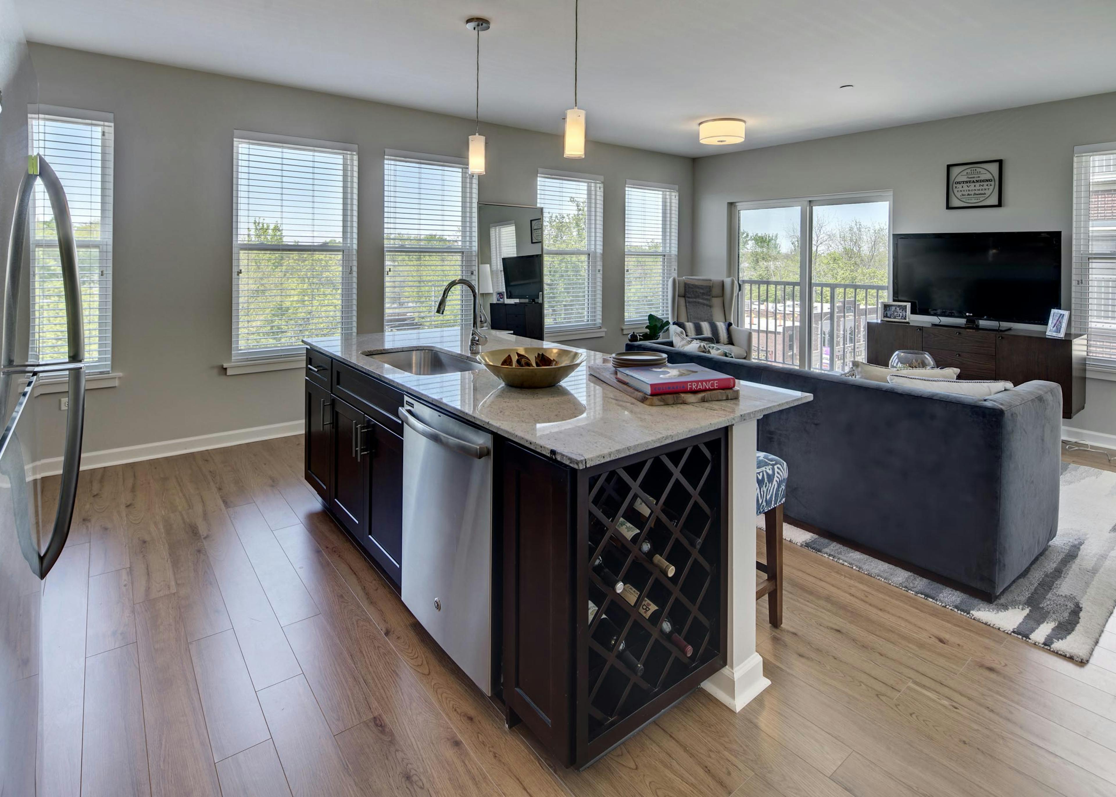 Sleek granite island in an AMLI Evanston apartment kitchen with view of living area in background surrounded by bright windows
