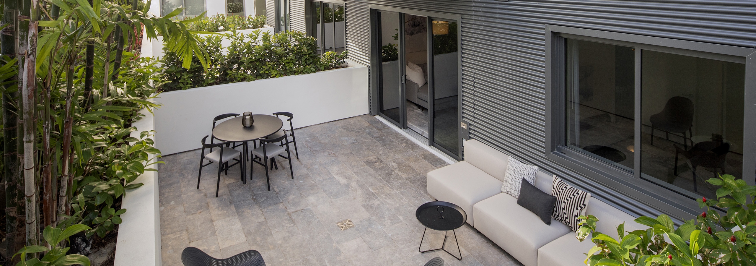 Daytime view of AMLI Midtown Miami apartment patio with table and chairs and other seating surrounded by lush landscaping