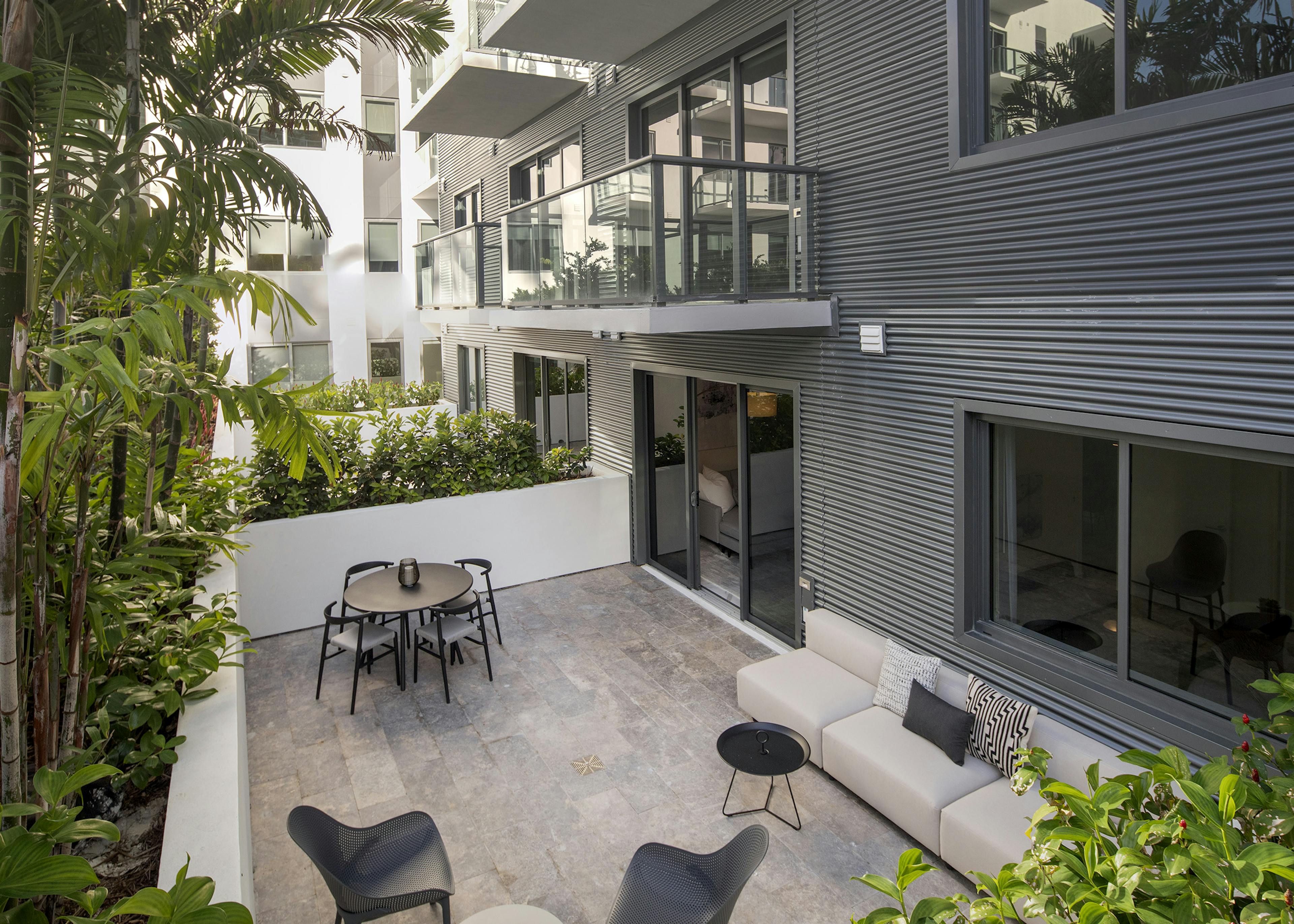 Daytime view of AMLI Midtown Miami apartment patio with table and chairs and other seating surrounded by lush landscaping
