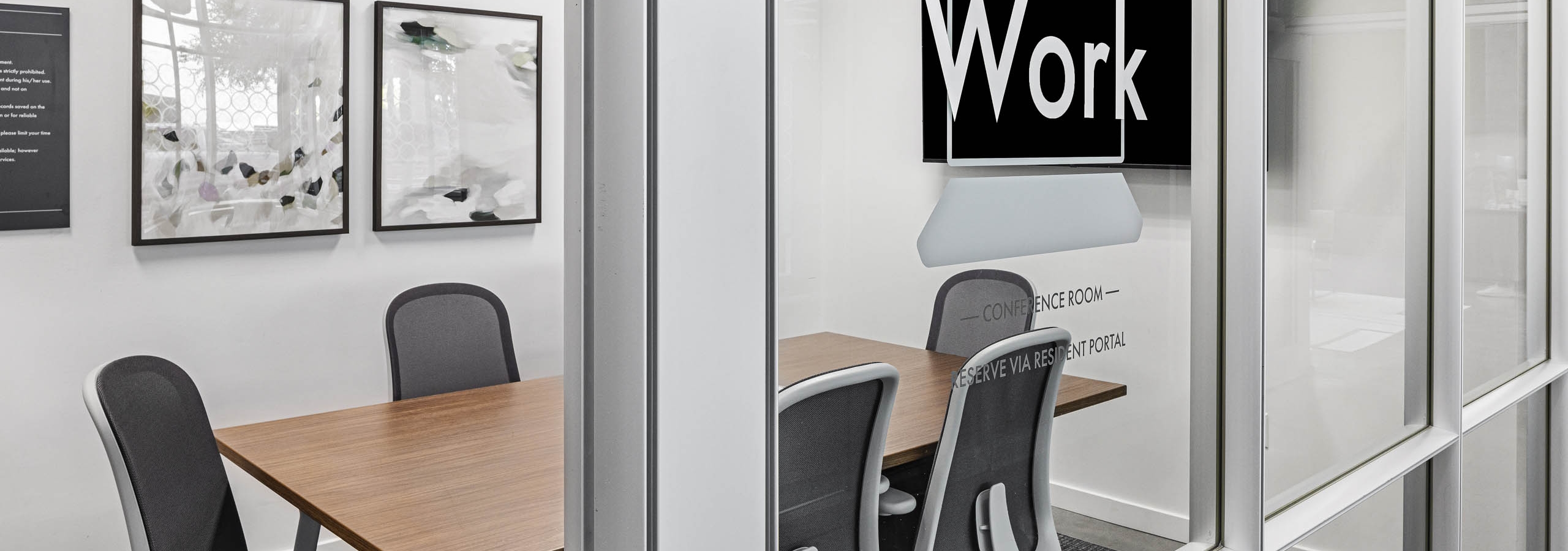 AMLI on 2nd conference room with glass wall and TV and artwork overlooking wood conference table and 6 black and white chairs