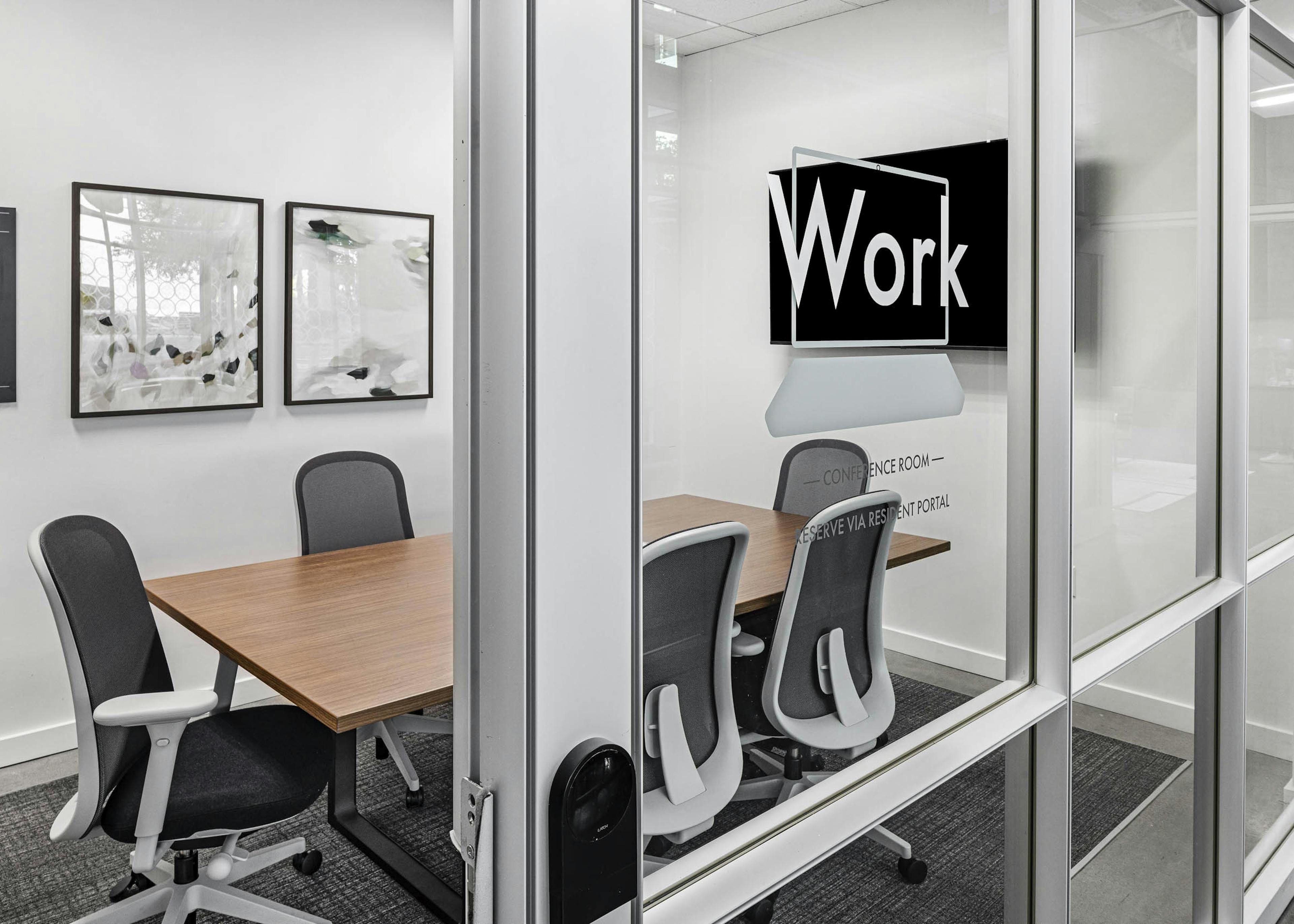 AMLI on 2nd conference room with glass wall and TV and artwork overlooking wood conference table and 6 black and white chairs