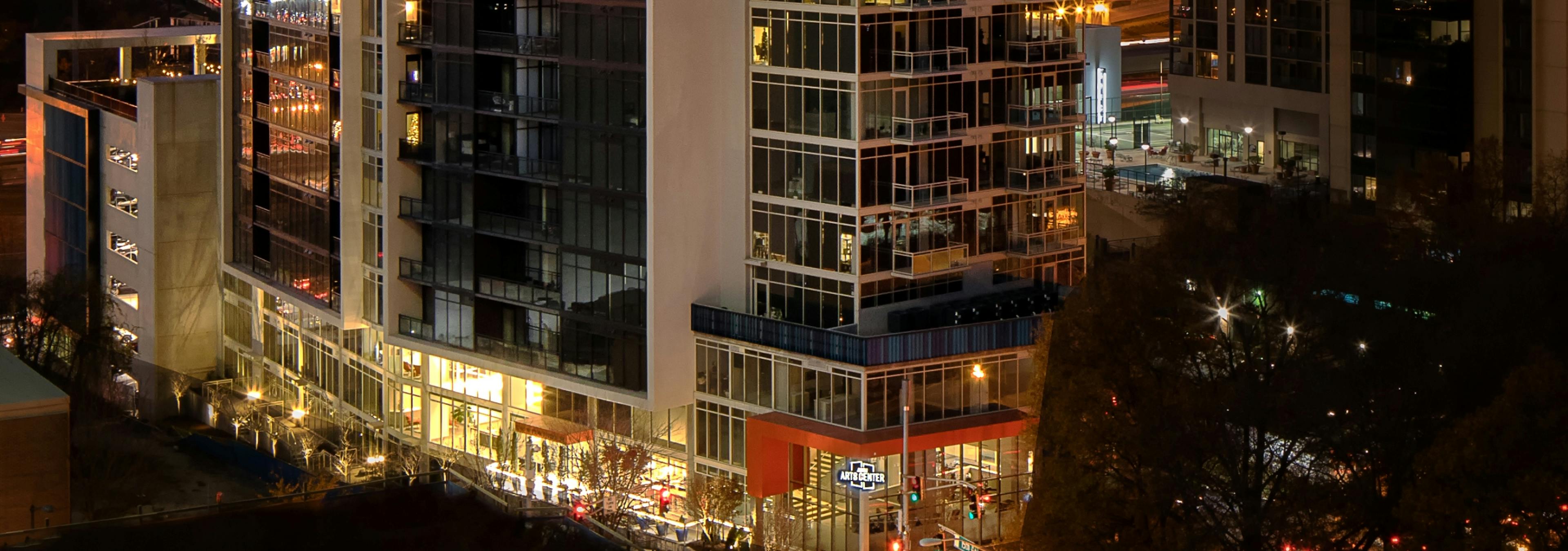Exterior of AMLI Arts Center apartment community building at night with windows on the lower floors shining bright light
