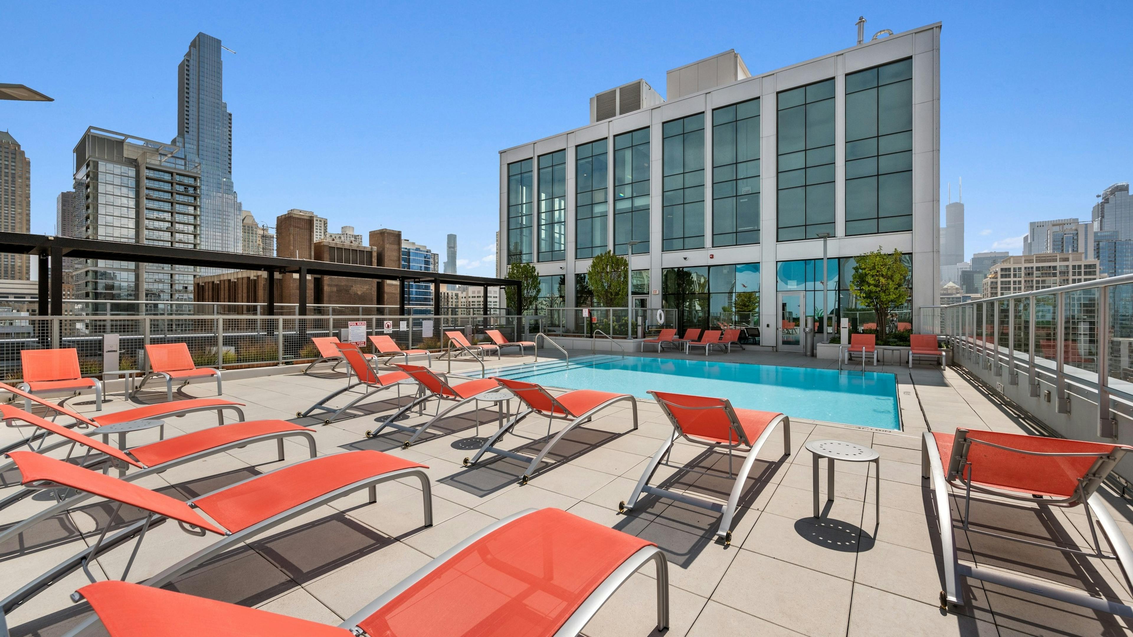 Luxurious rooftop pool at AMLI 808 apartment building with orange lounge chairs surrounded by stunning Chicago skyline views