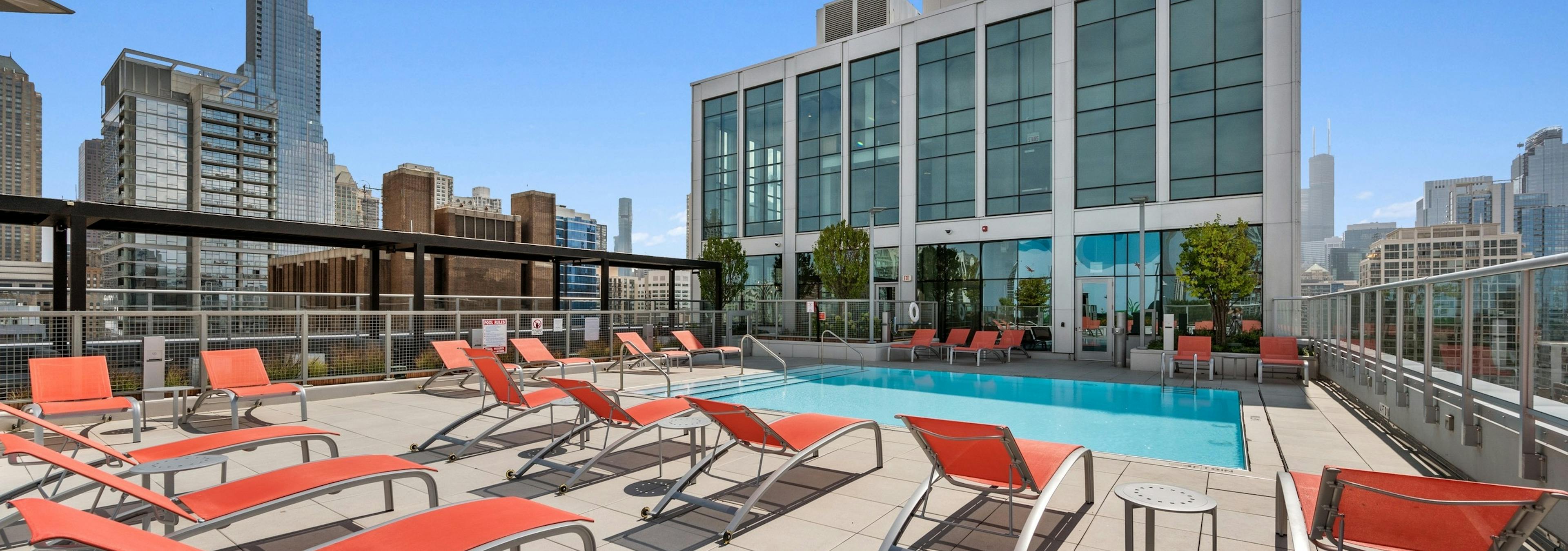 Luxurious rooftop pool at AMLI 808 apartment building with orange lounge chairs surrounded by stunning Chicago skyline views