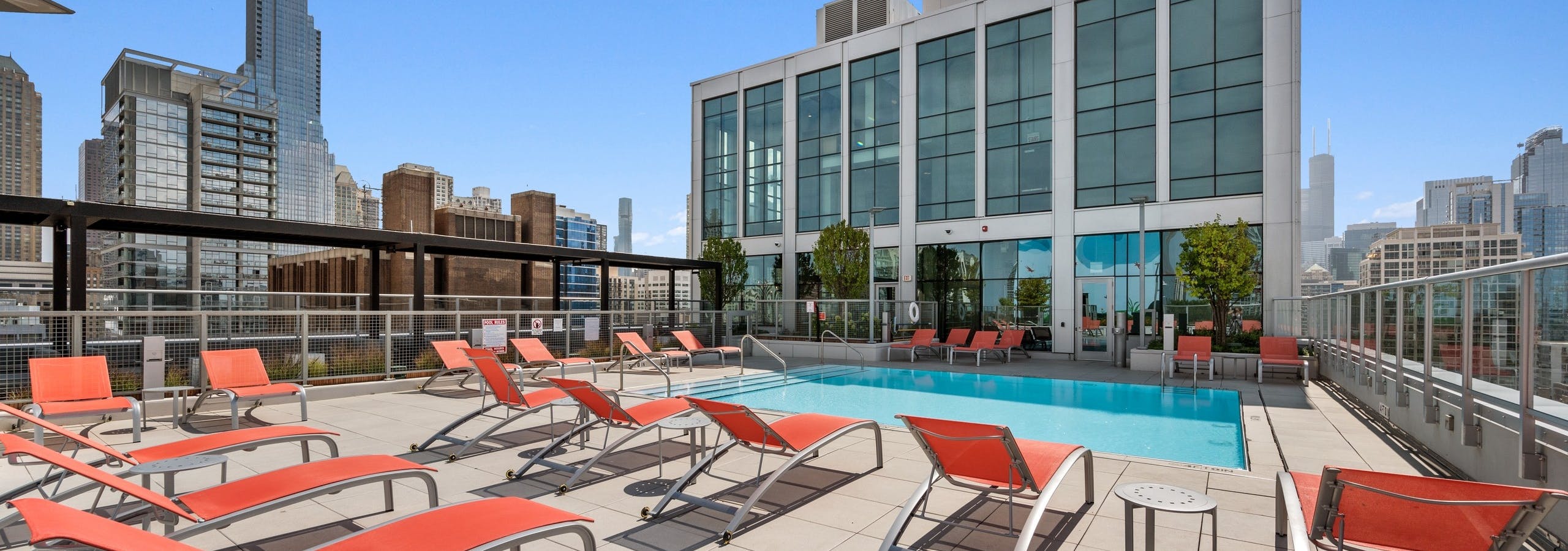 Luxurious rooftop pool at AMLI 808 apartment building with orange lounge chairs surrounded by stunning Chicago skyline views