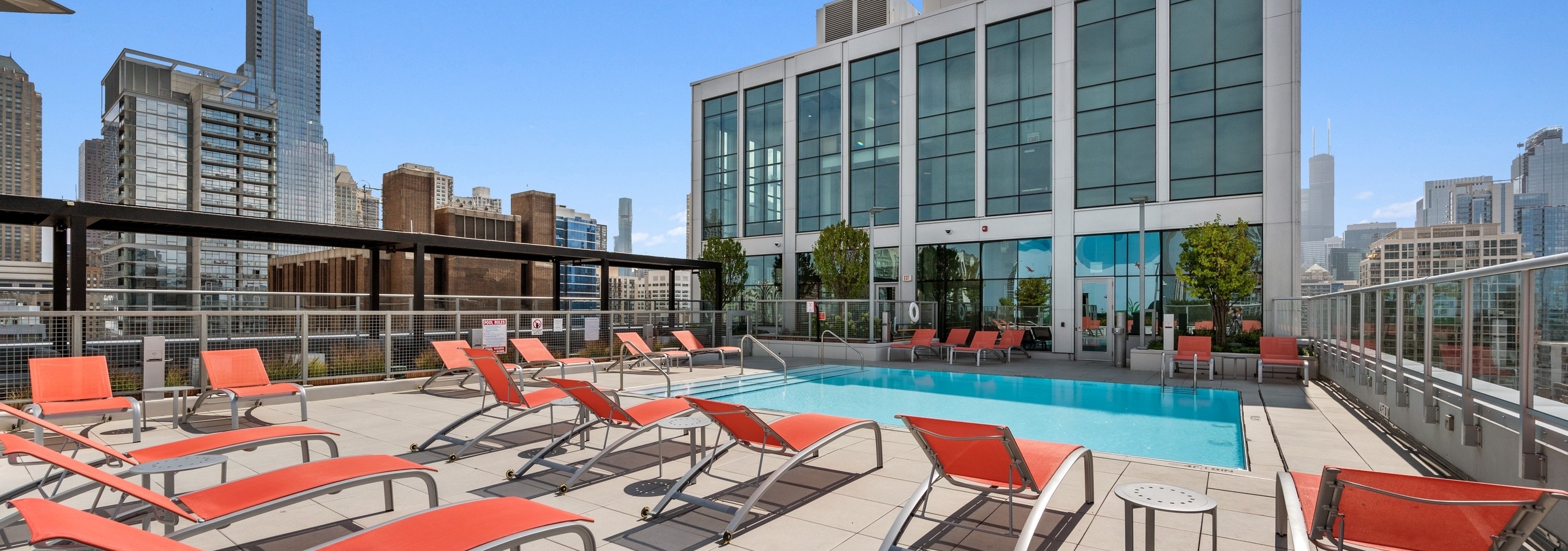 Luxurious rooftop pool at AMLI 808 apartment building with orange lounge chairs surrounded by stunning Chicago skyline views